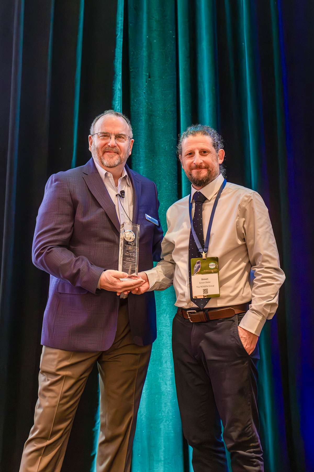 This photo shows the ceremonial presentation of the PRCI Researcher Award to Simon Slater on stage.