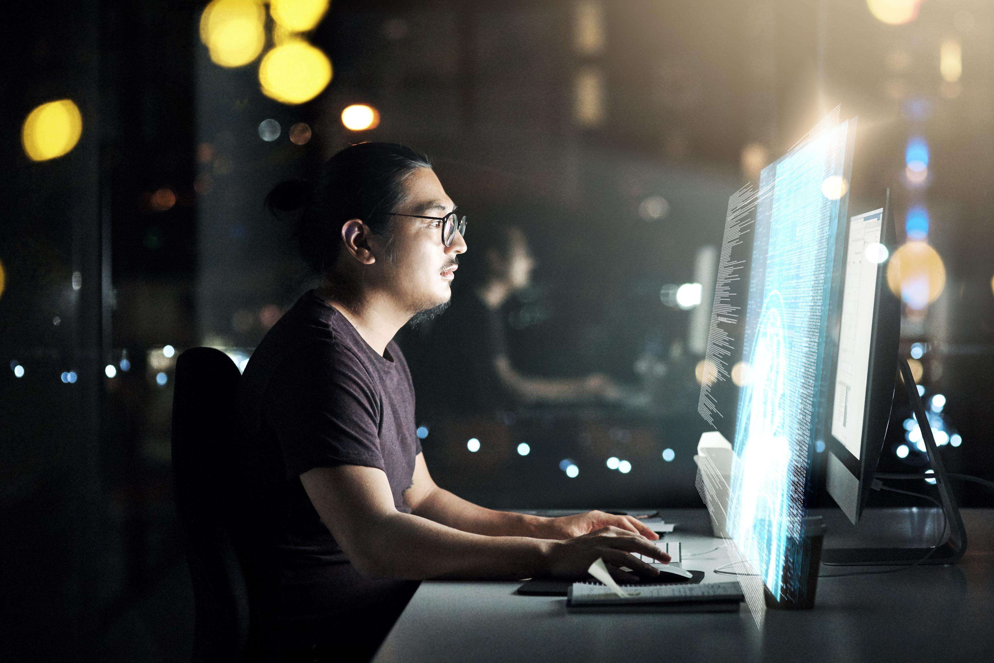 Side portrait of a man wearing glasses and sitting in front of several monitors.