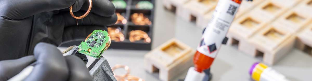 Zwei behandschuhte Hände verrichten beim Zusammenbau der Sensoren eine äußerst filigrane Arbeit.