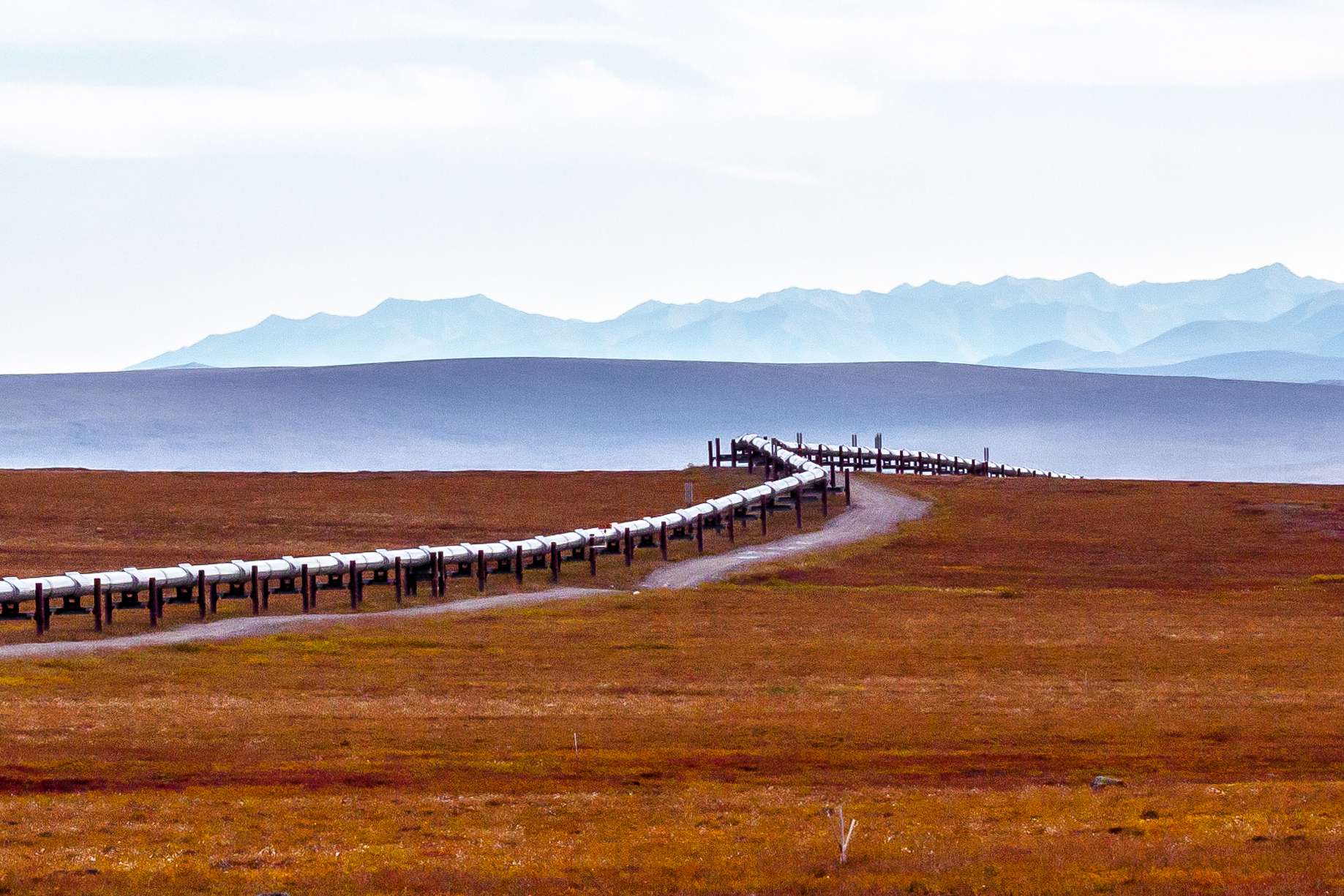 Image of above ground pipeline going through flat landscape with mountains in the background.