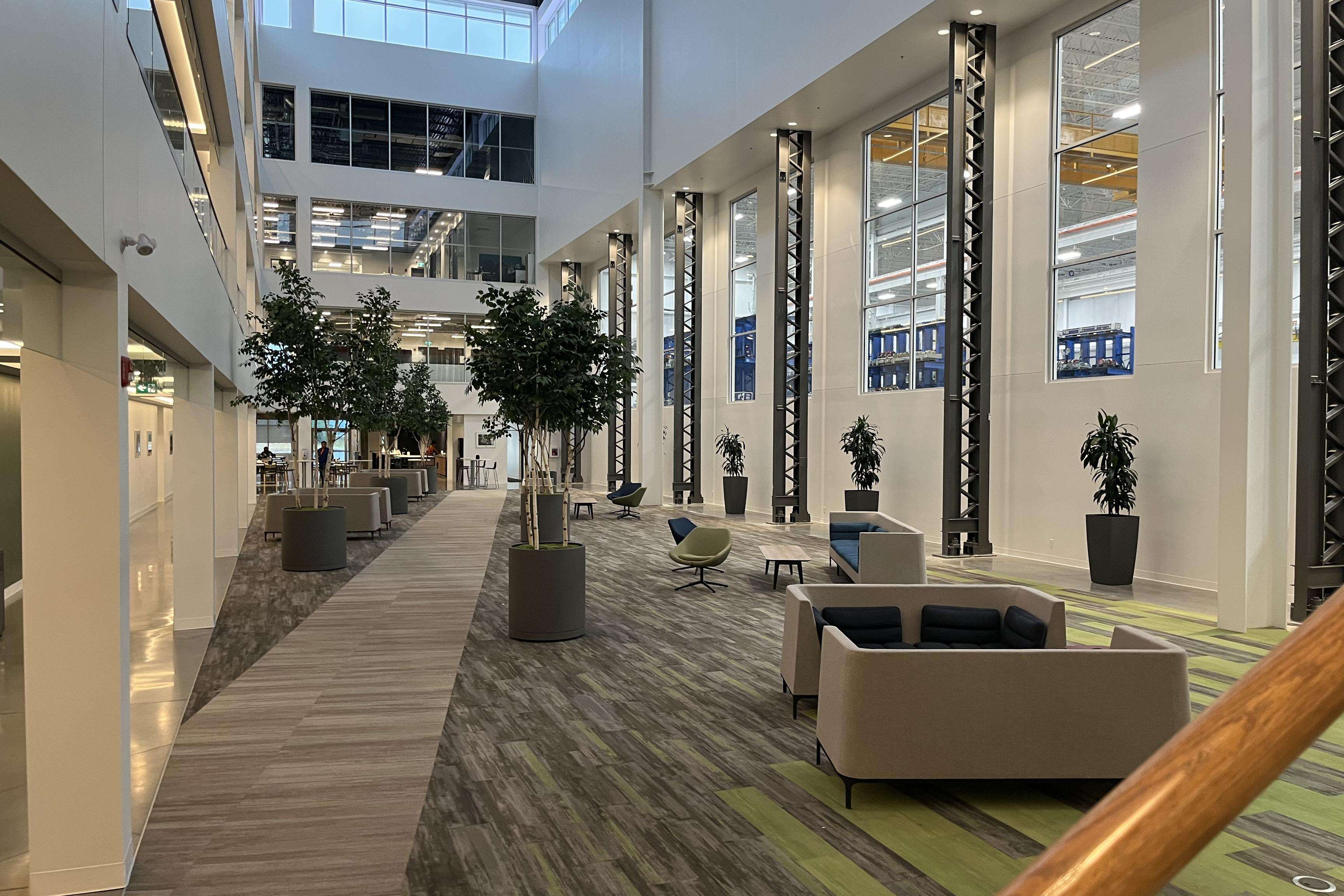 Light-flooded atrium kept in white, gray, green with seating and view into the production.