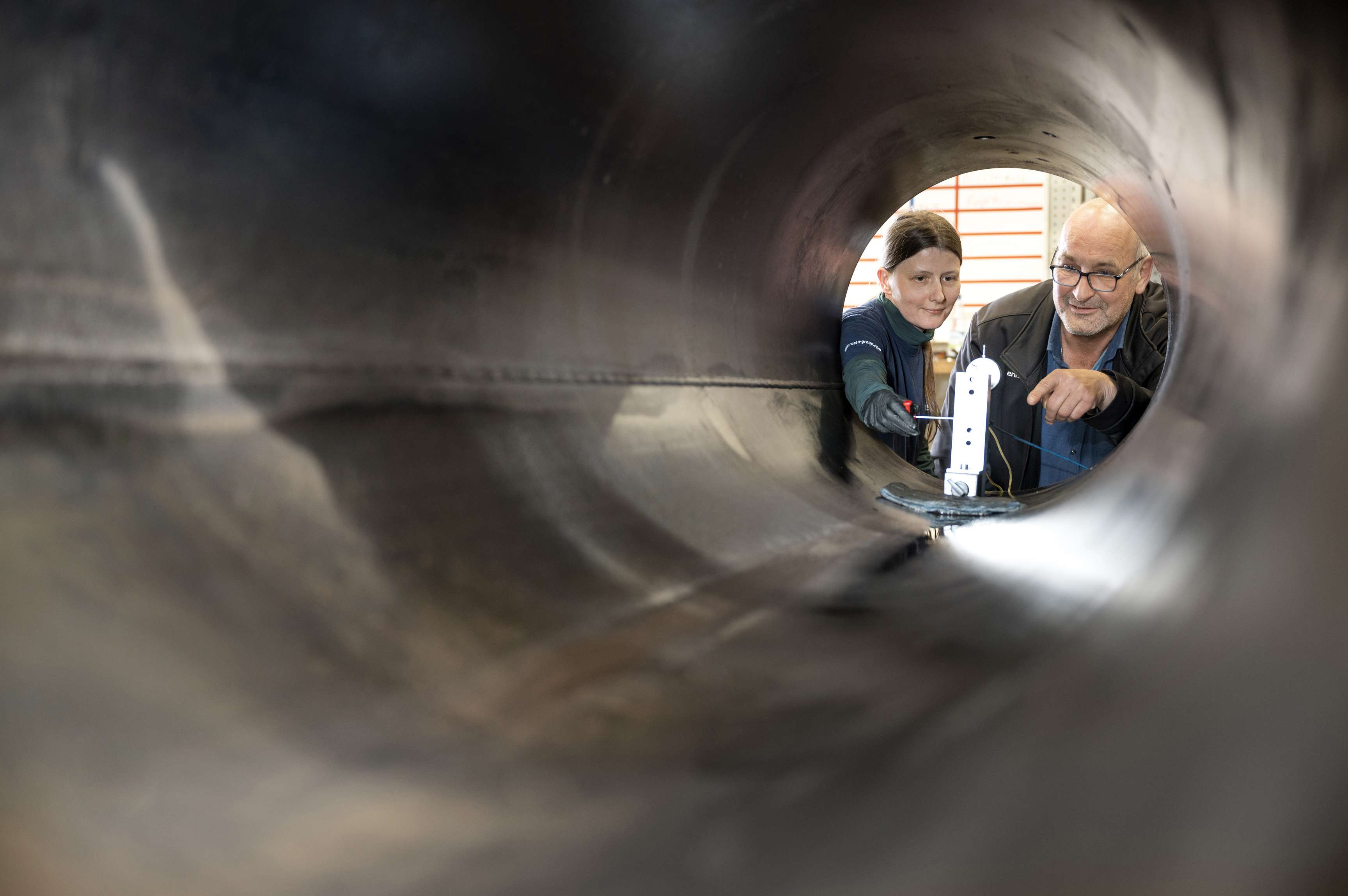 View from inside a pipeline of two employees looking at a device inside the pipeline.
