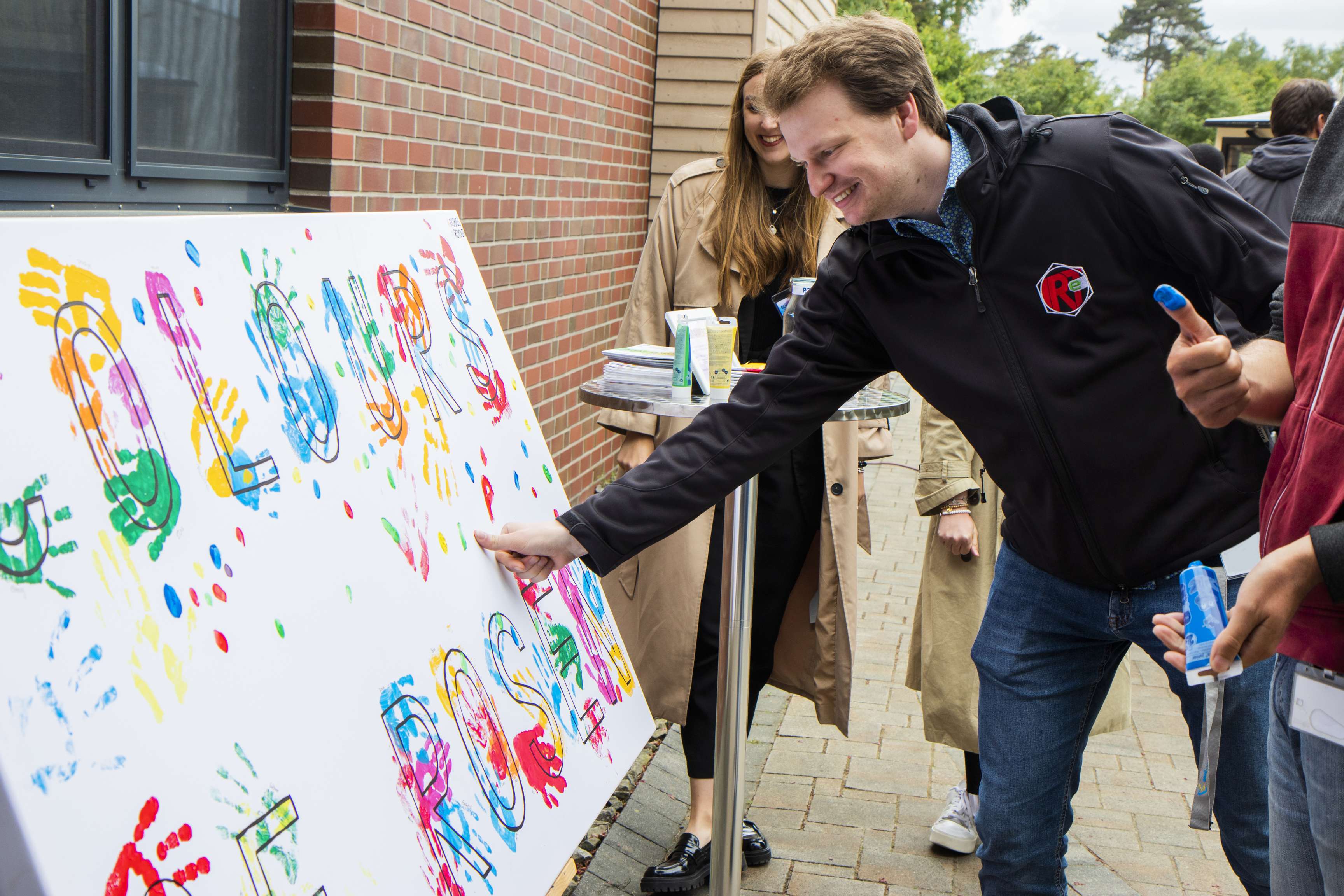 Man placing his inked thumb on a poster with many colored fingerprints and handprints and the slogan Colors of ROSEN.