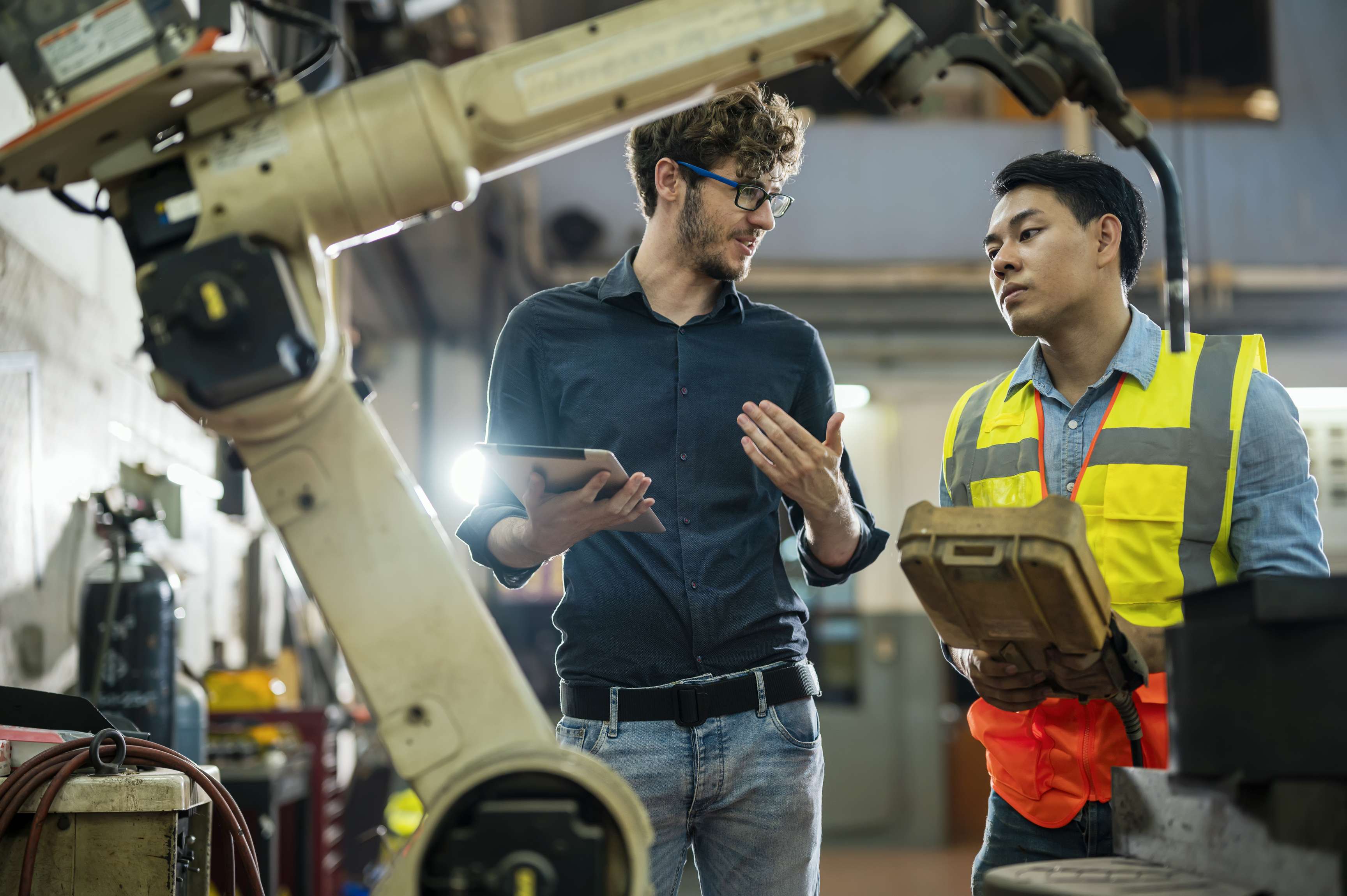 Two men talking to each other and standing next to a robot arm.