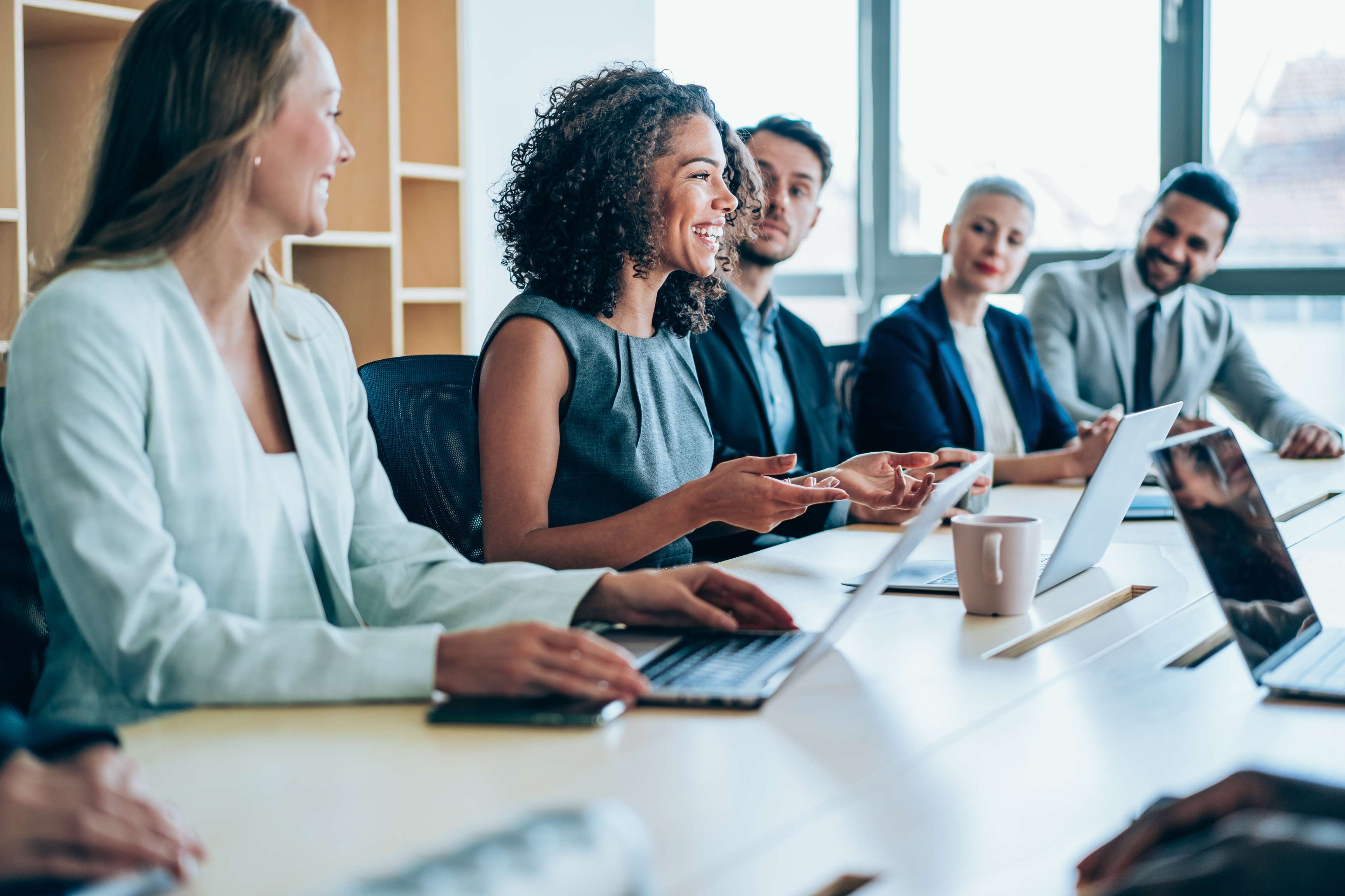 Several employees have a meeting in a conference room and look at a screen in front.