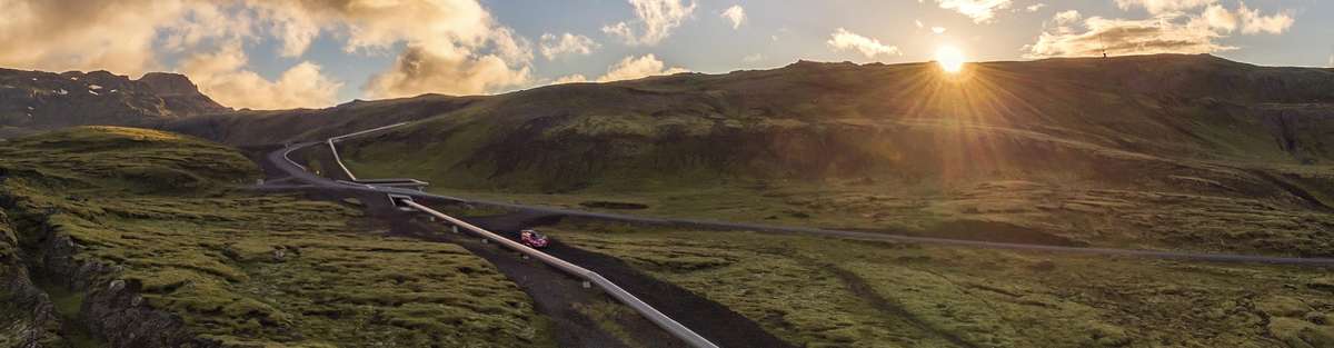 Pipeline running through a slightly hilly, green landscape, with the sun shining.