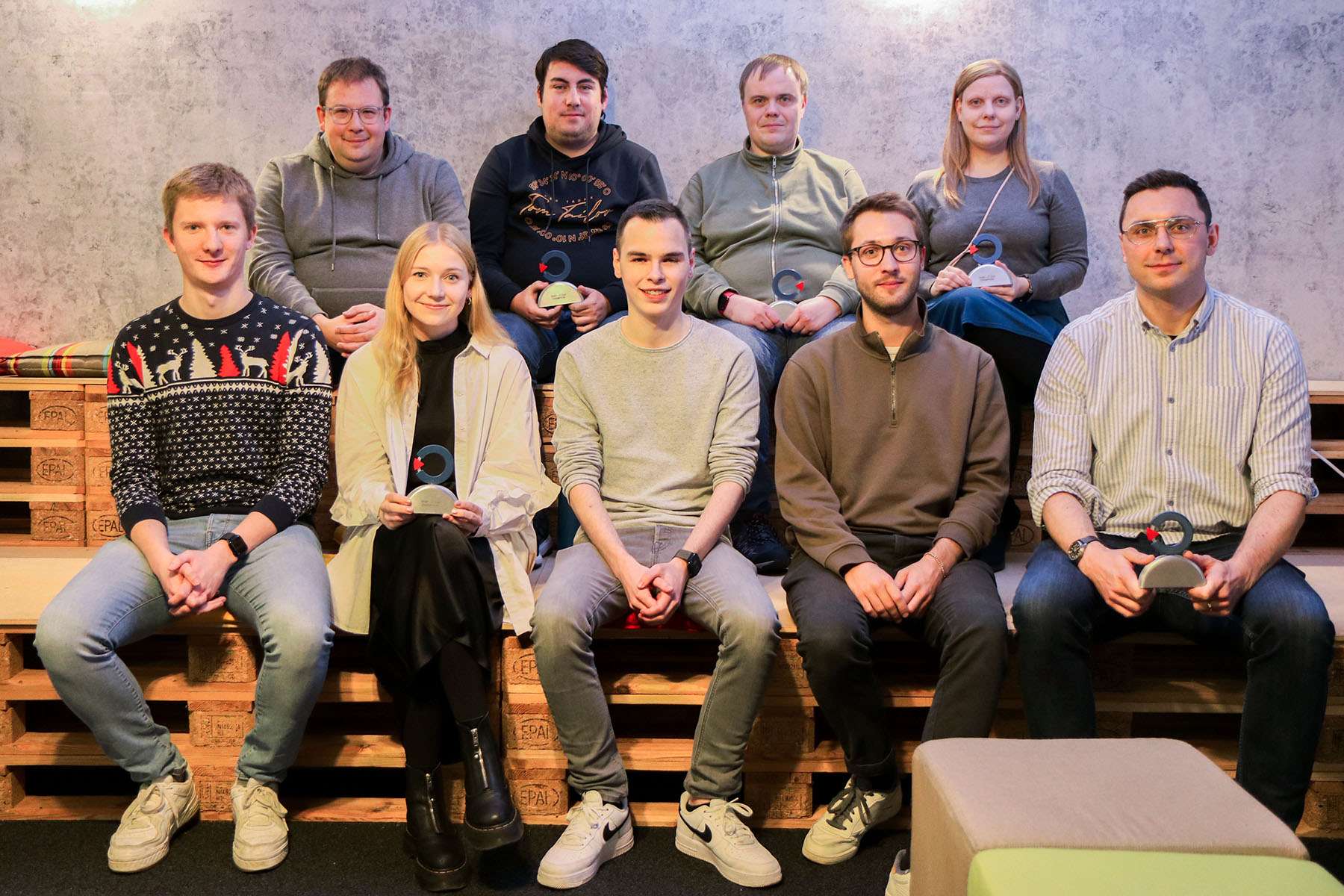 A group of people are sitting together for a group photo. Some of them are holding small awards.