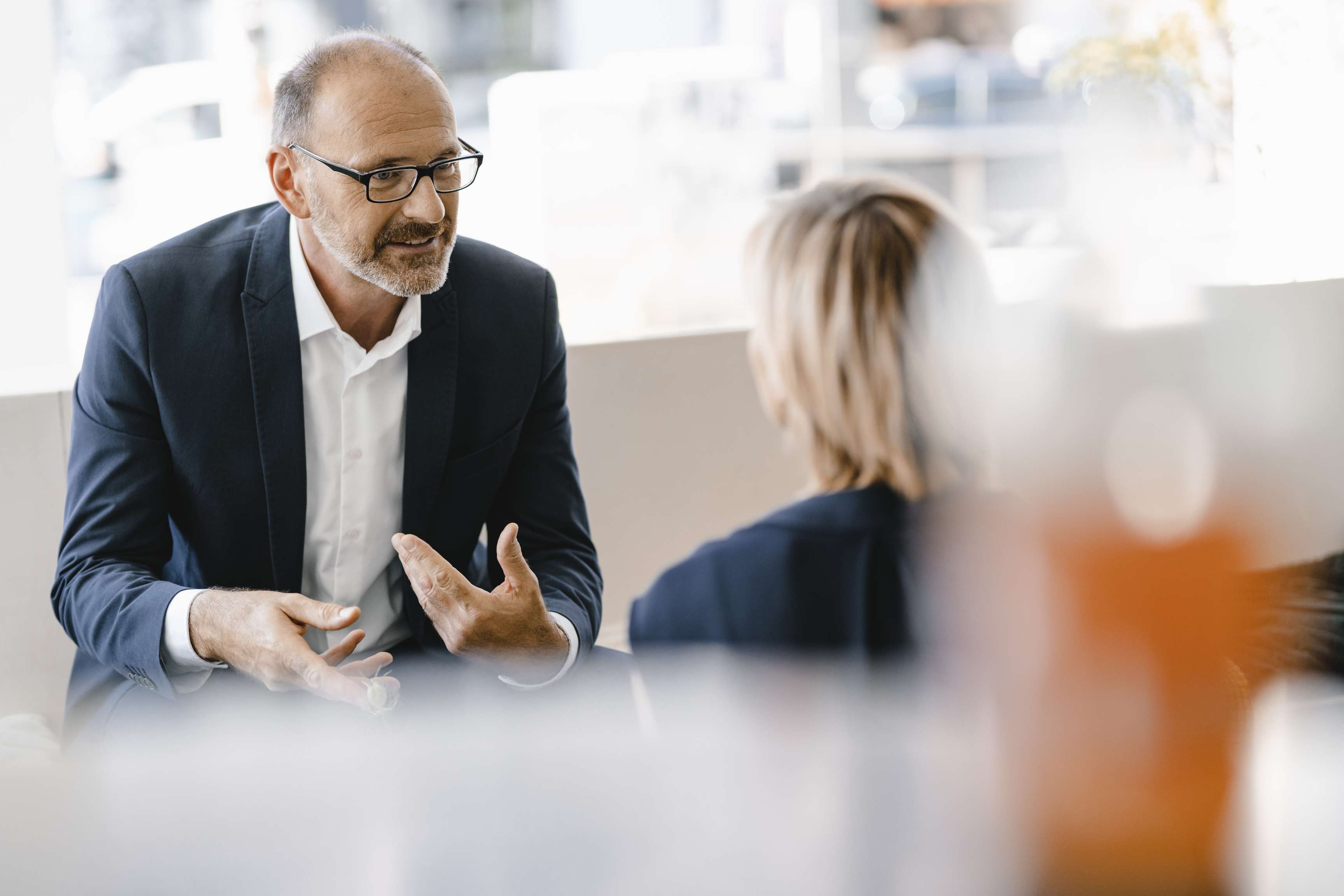 A man and a woman sit across from each other in a meeting and talk about their work.