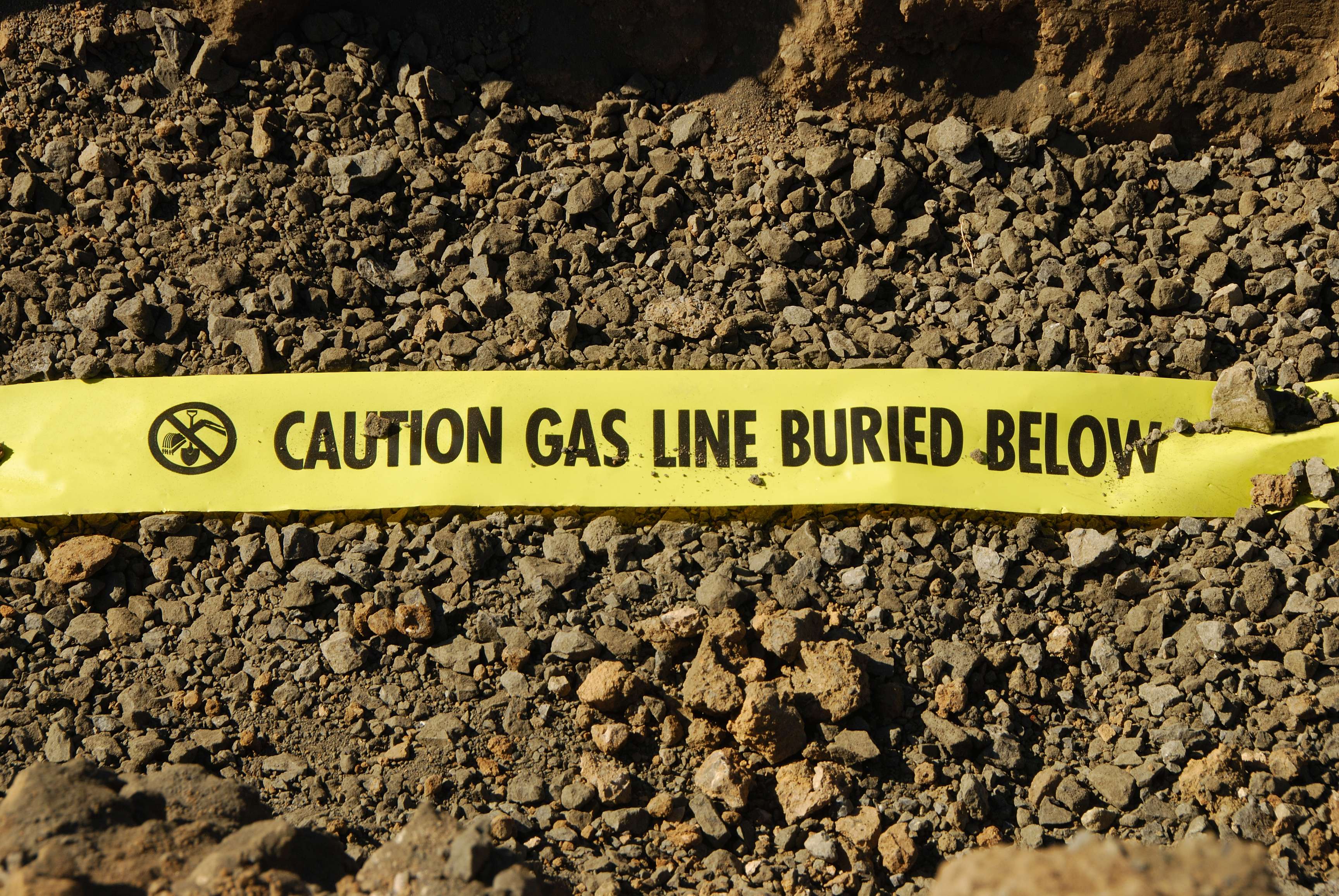 Yellow warning tape warns of a gas line under the earth.