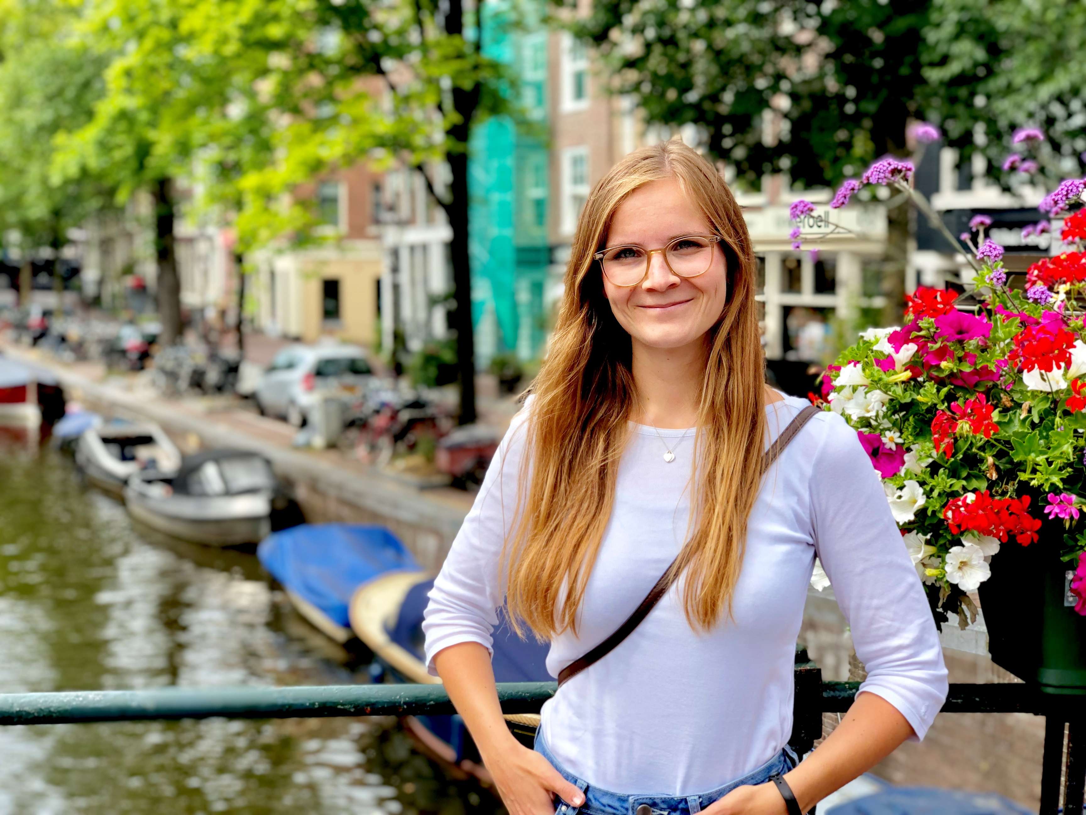 Young smiling woman with glasses in front of canals in Amsterdam.