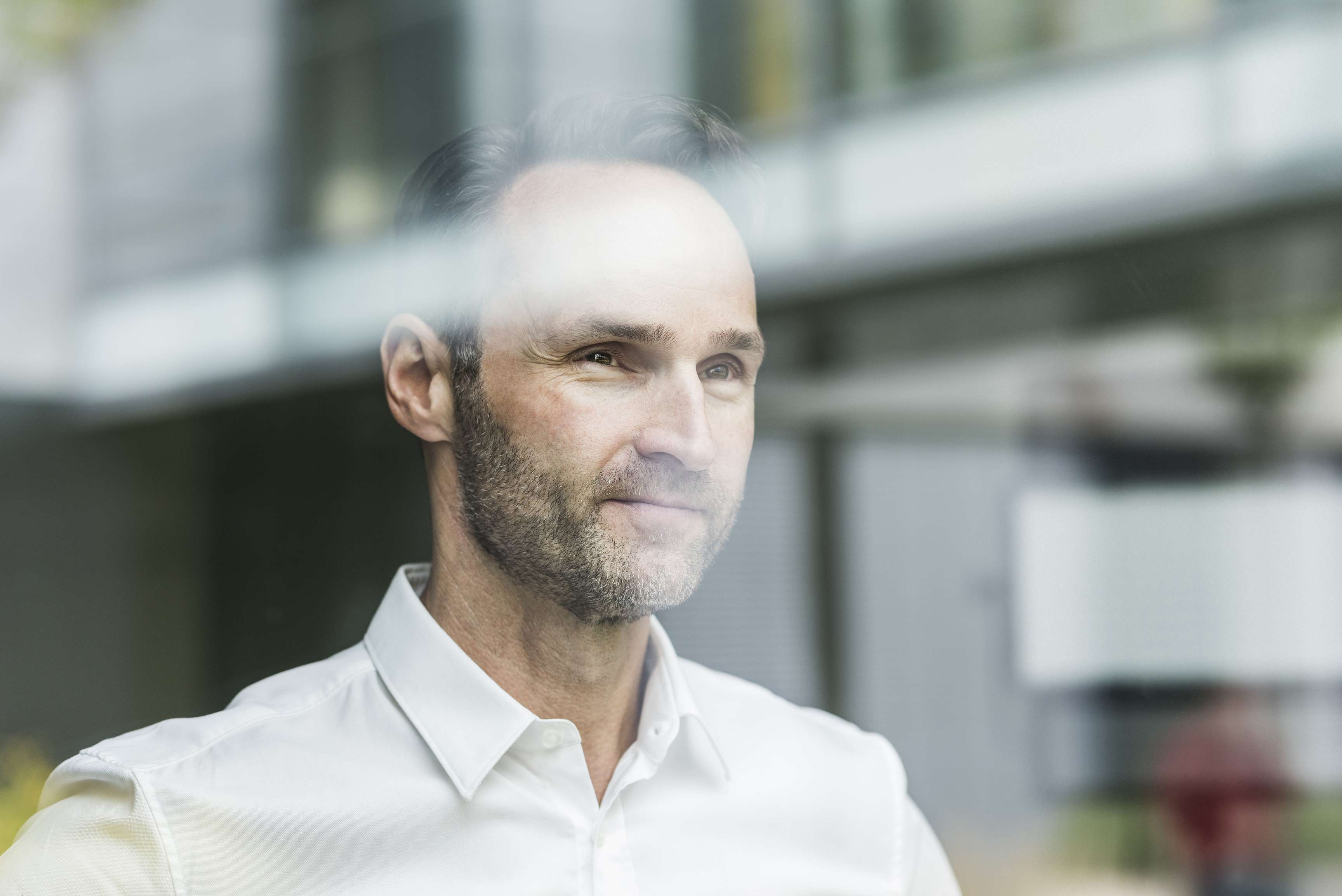 A man smiling while looking through a window into the distance.