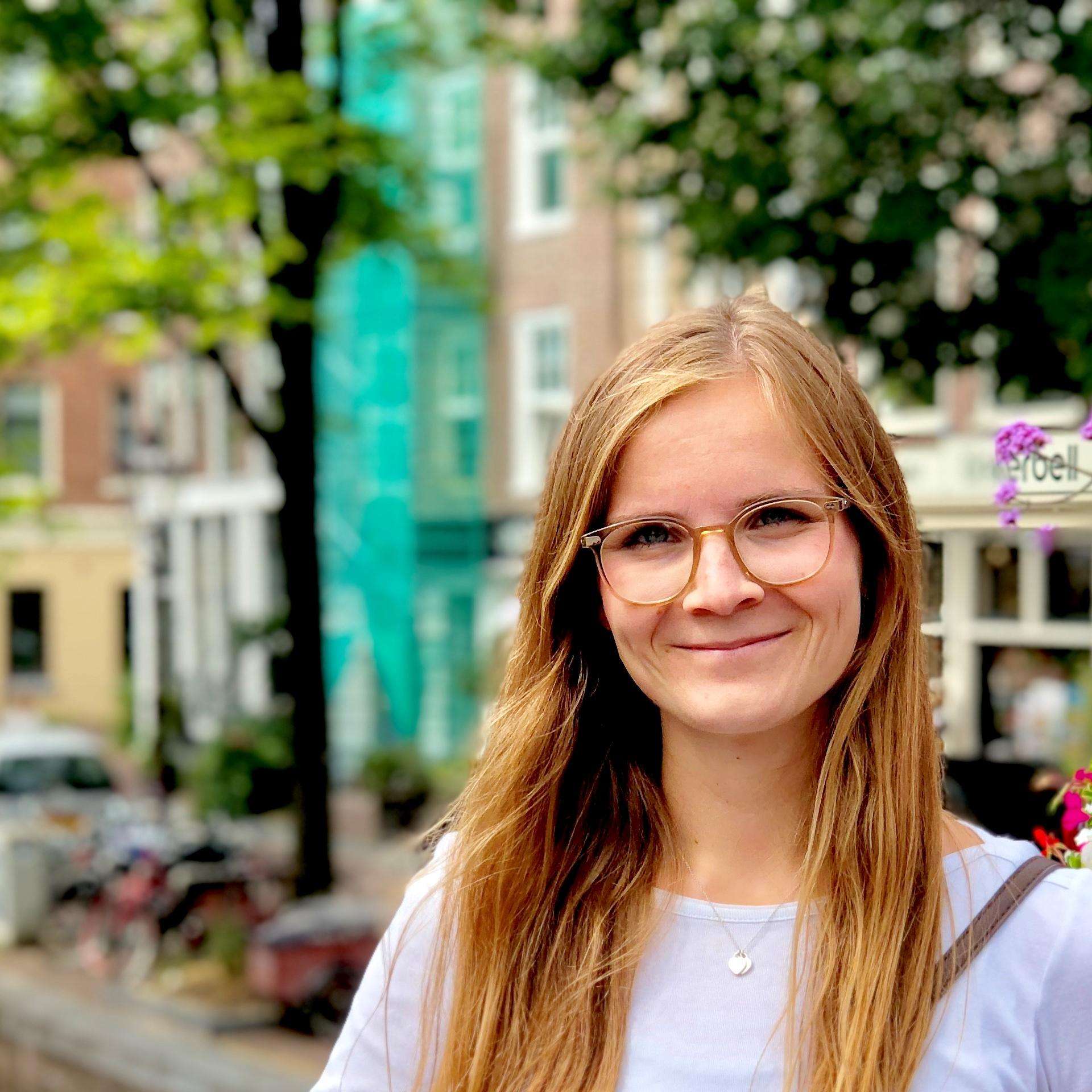 Young smiling woman with glasses in front of canals in Amsterdam.