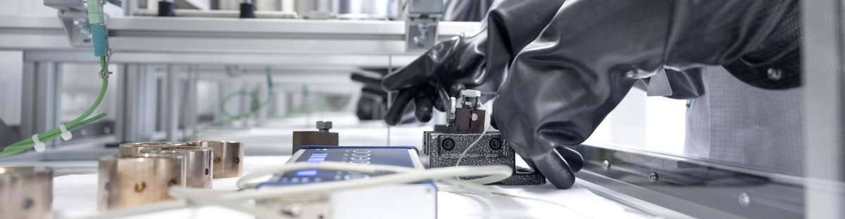 Black work gloves in front of a display connected to a device in a laboratory.