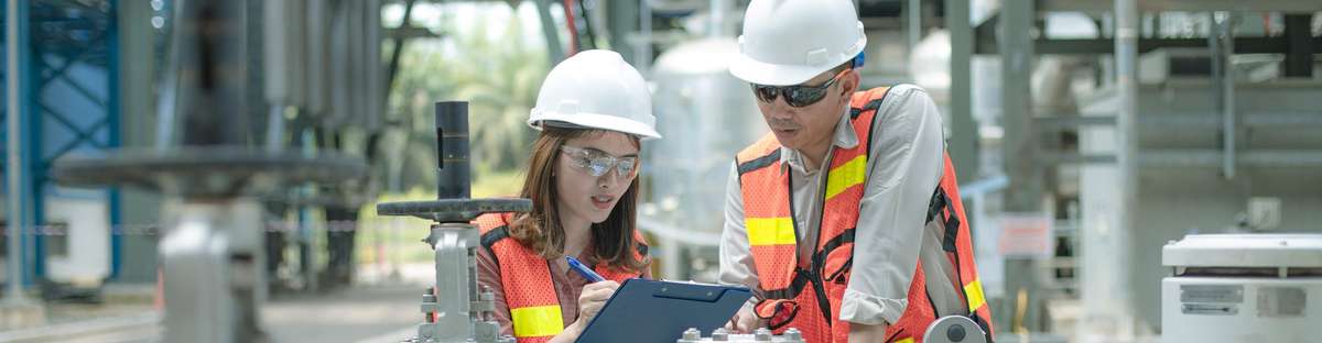 Two employees with protective equipment work together on a clipboard.