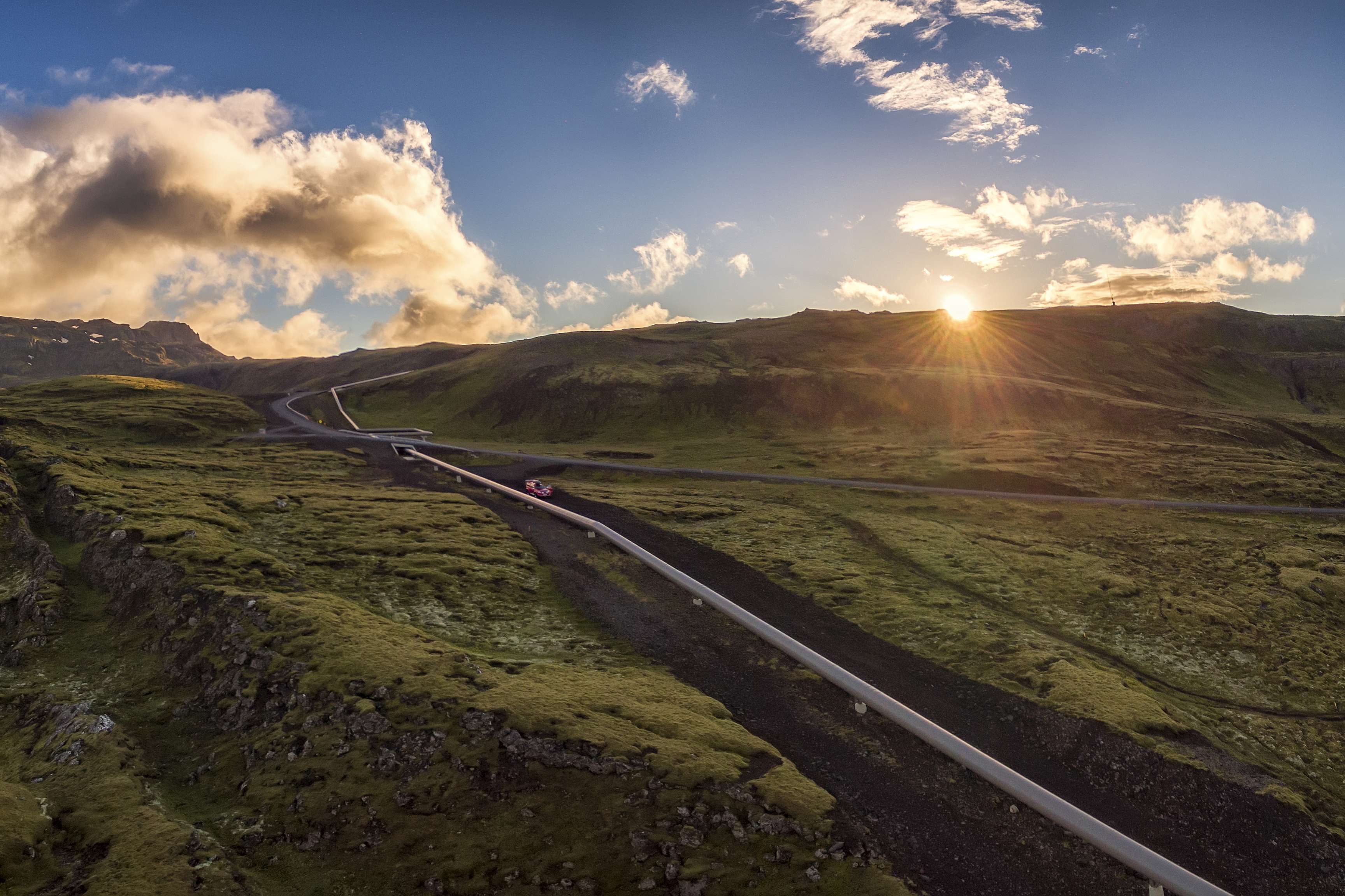 Pipeline running through a slightly hilly, green landscape, with the sun shining.