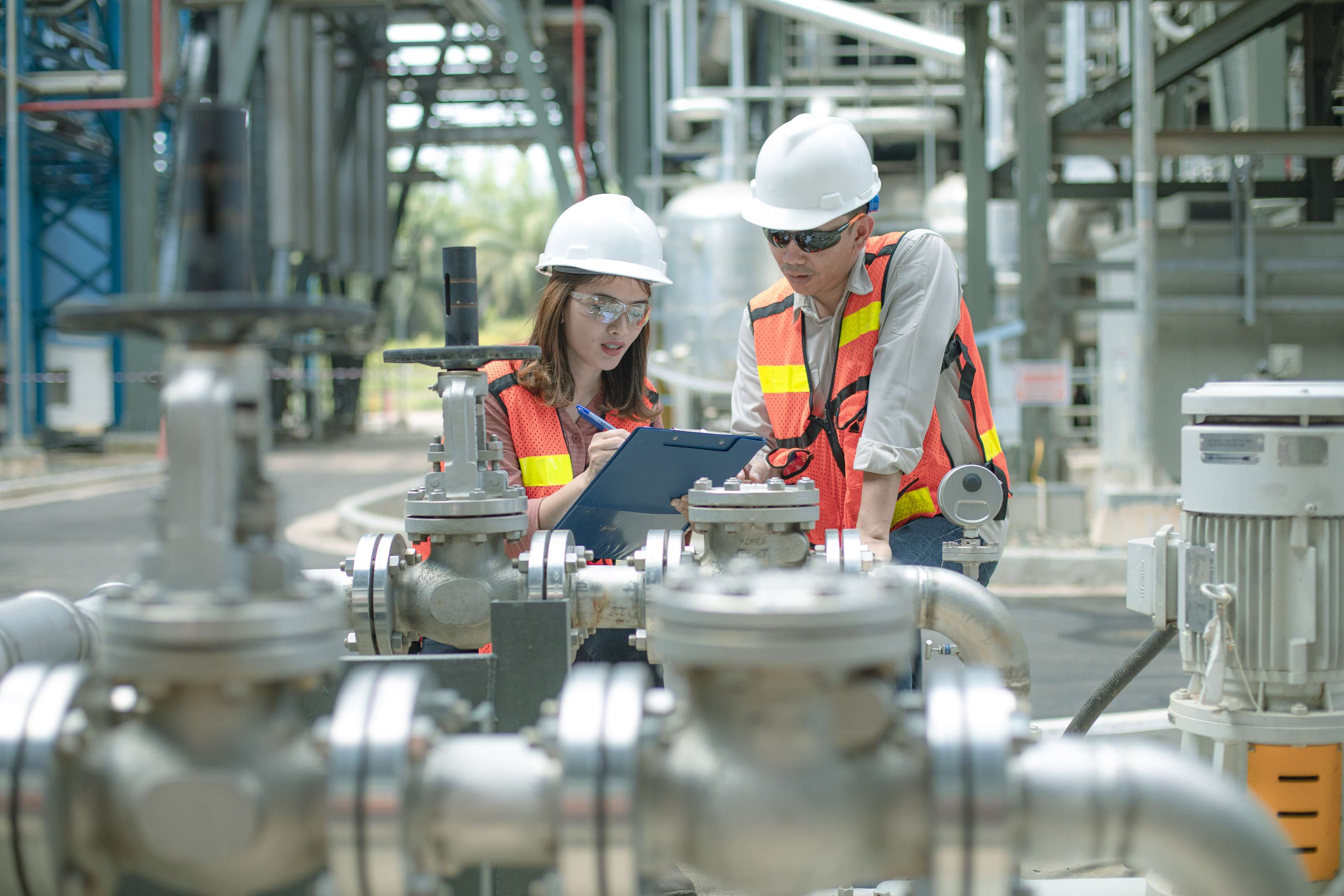 Two employees with protective equipment work together on a clipboard.