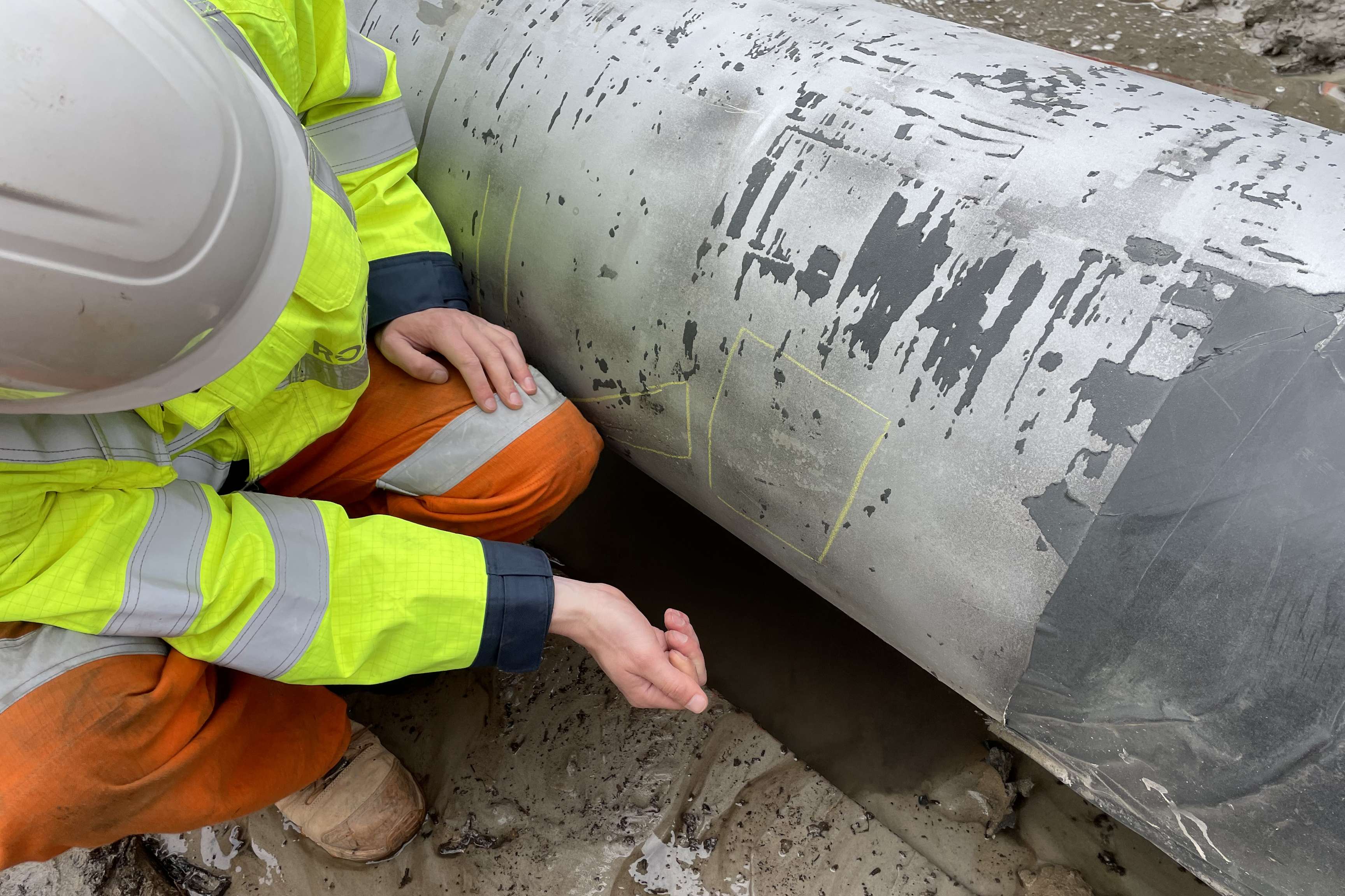 Close-up of an employee inspecting the damaged coating of a pipeline.