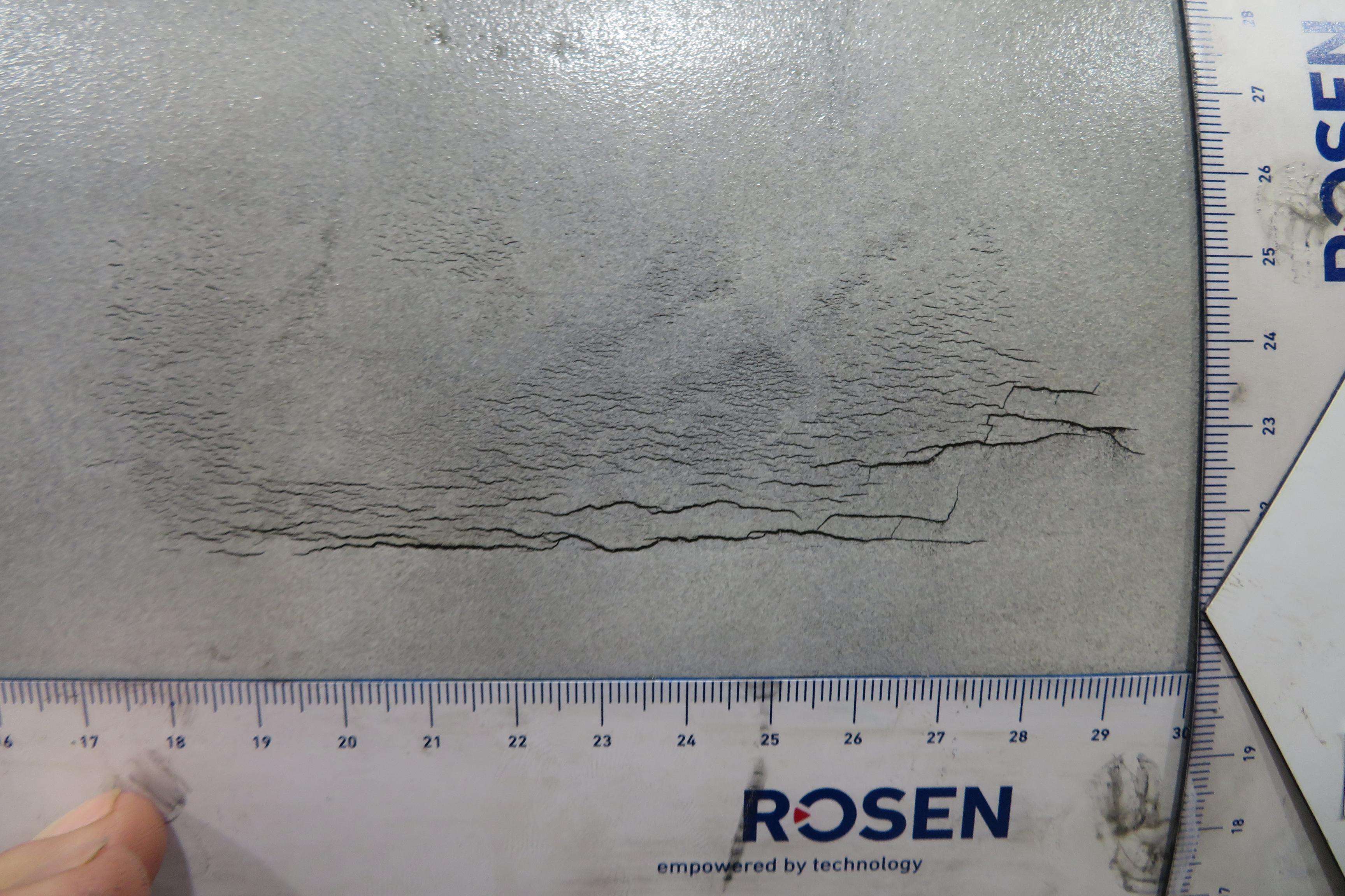 Detailed picture with cracks on a pipeline and measuring rulers on the side.