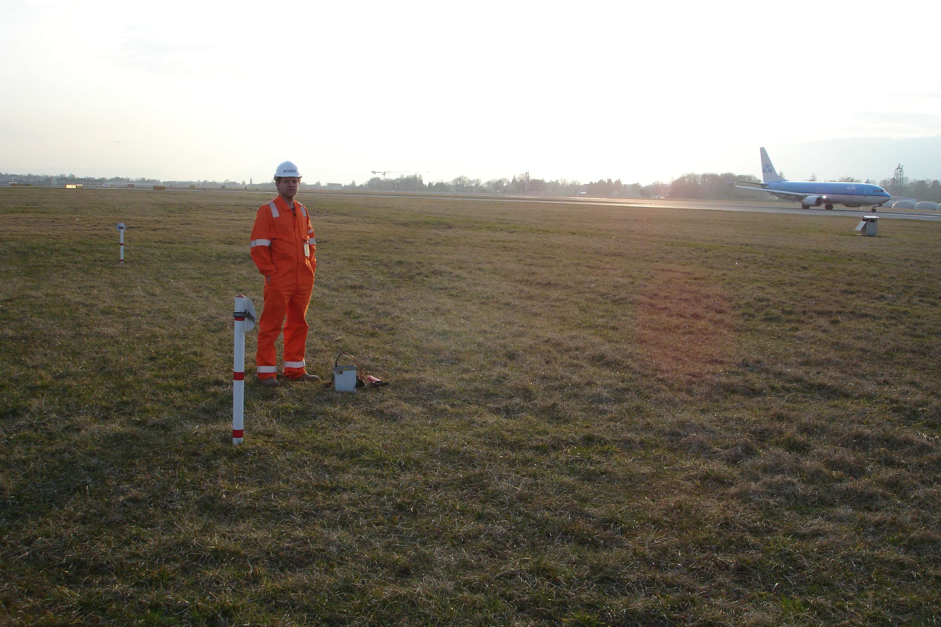 Worker with helmet on a grassy area next to a runway.