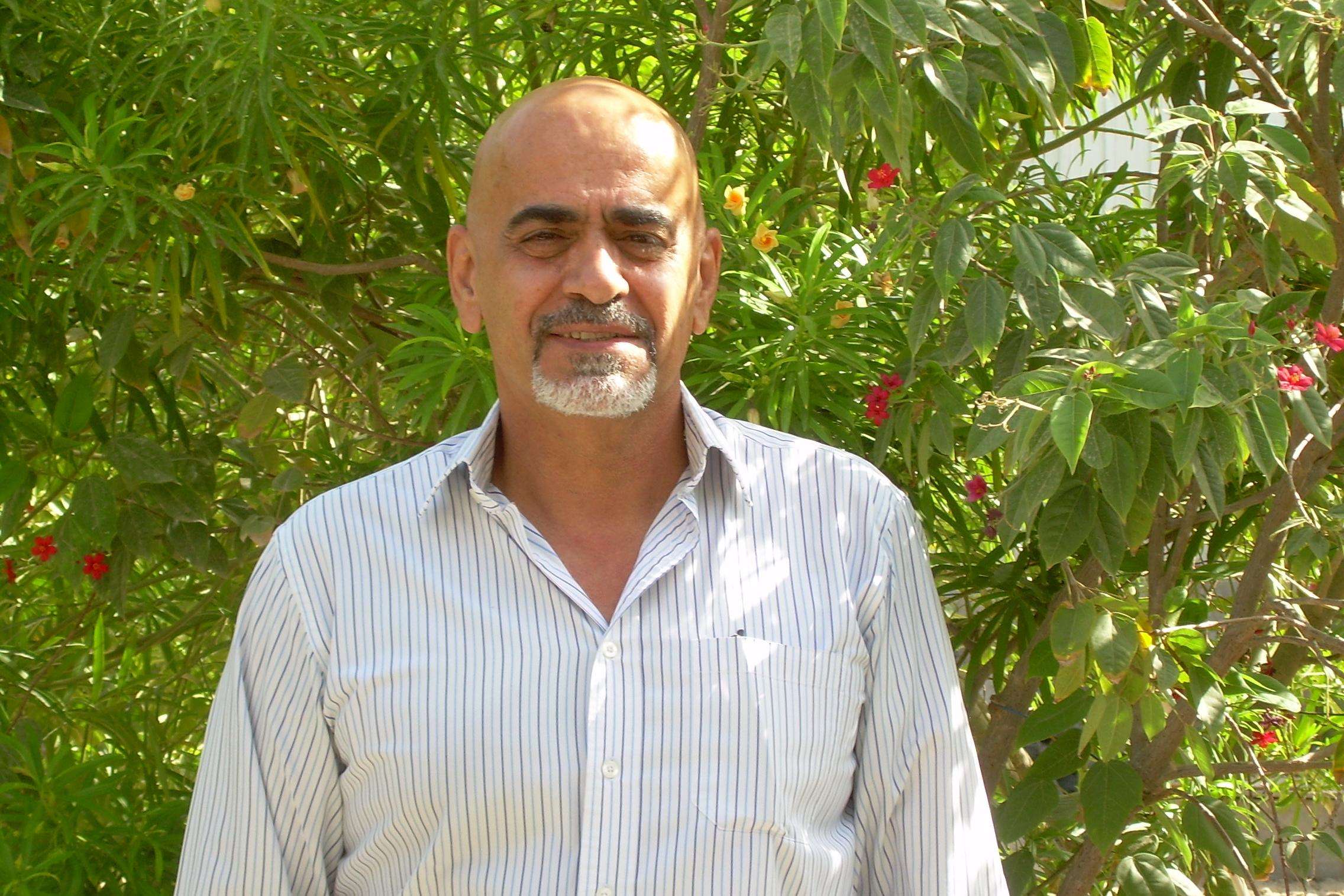 Man smiling into camera as portrait standing in front of leaves.