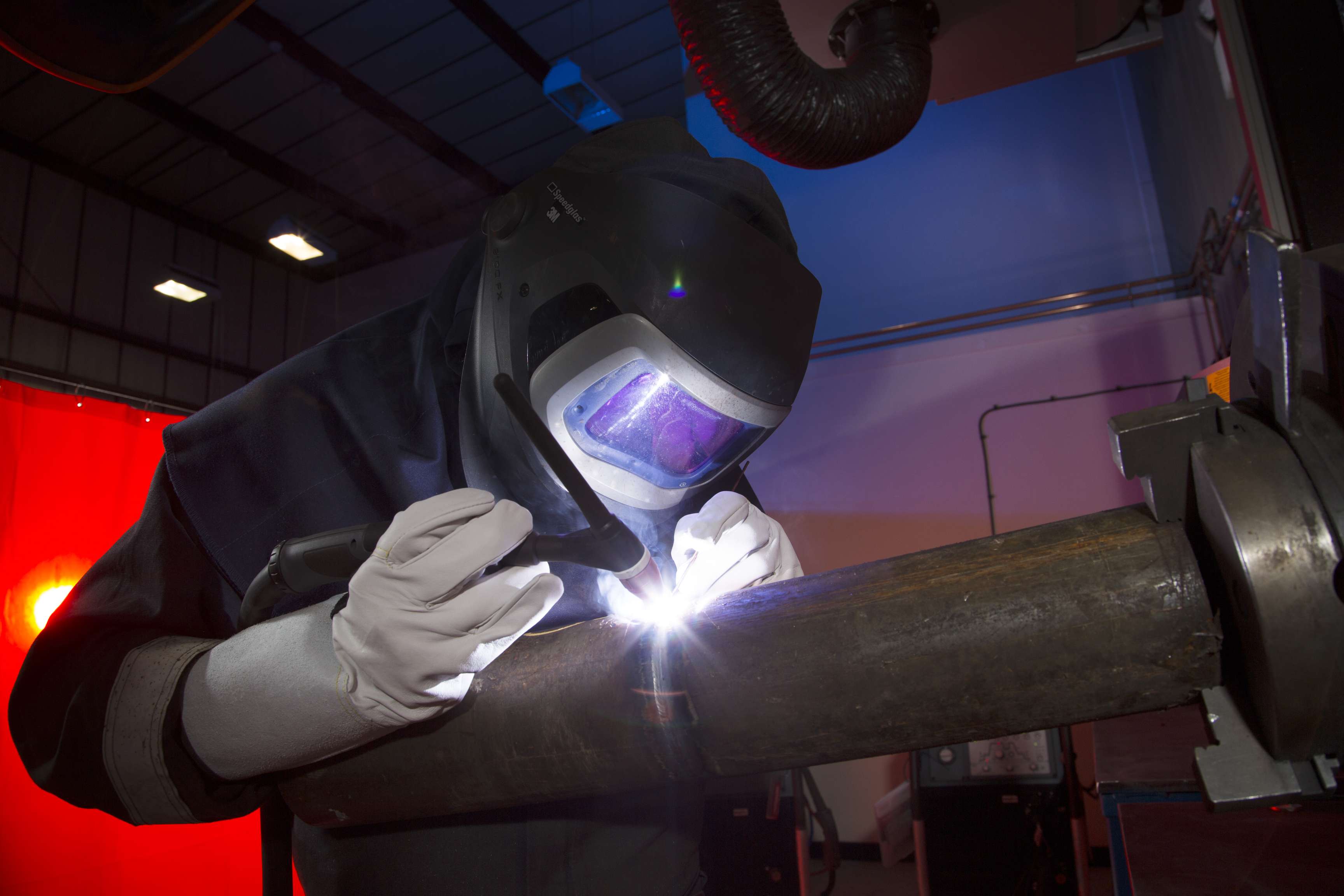 Employee with helmet and protective equipment welding on a pipeline.