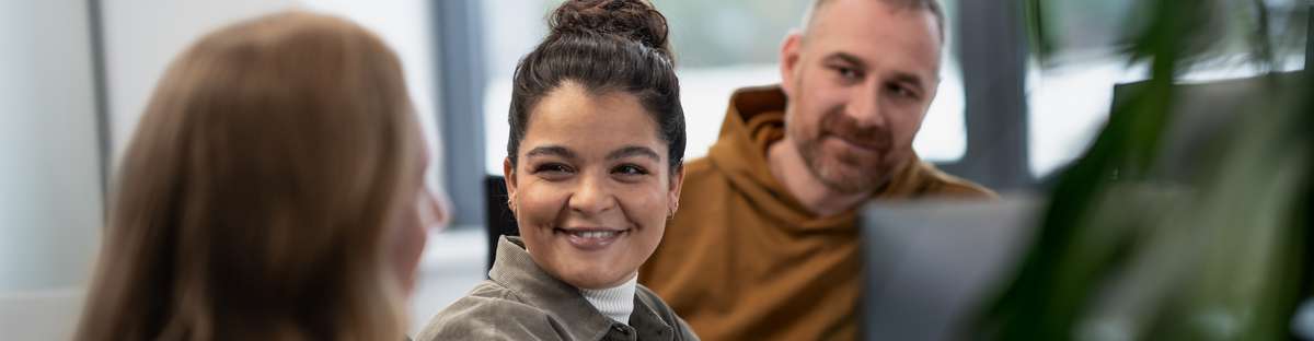 Zwei Frauen und ein Mann sitzen an einem Schreibtisch und unterhalten sich.