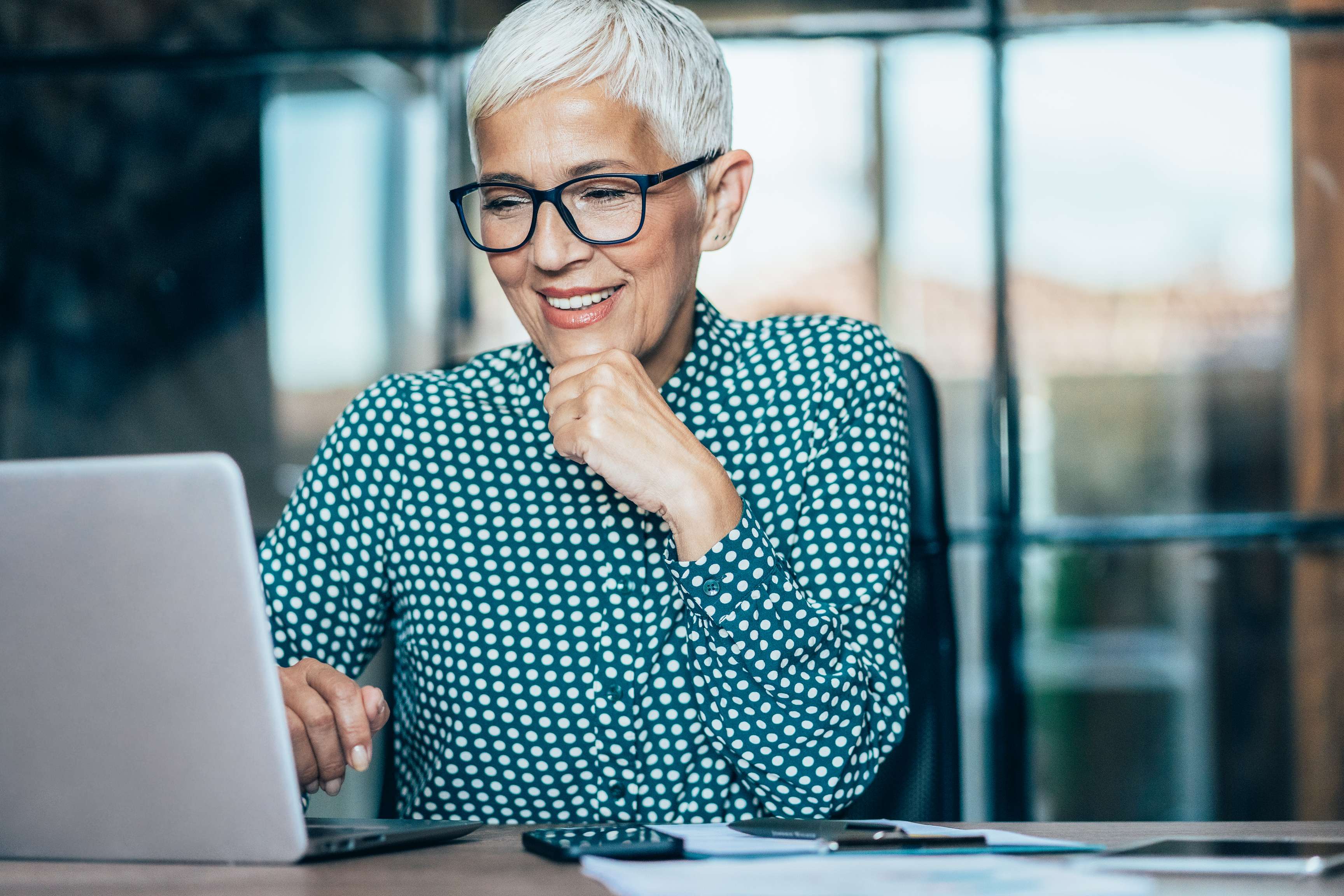 Woman wearing glasses and smiling sitting in front of laptop.