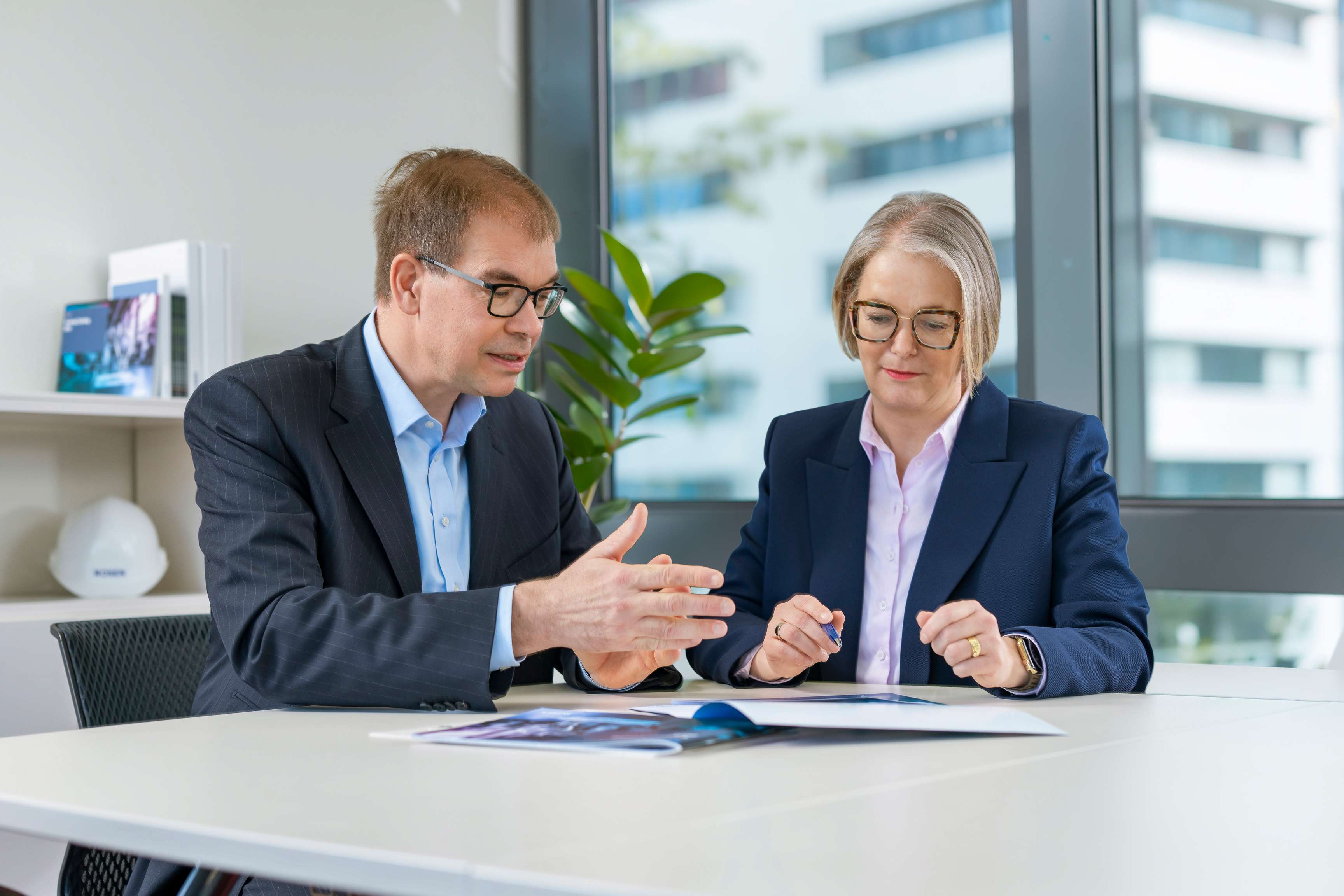 The picture shows Andreas Opfermann and Daniela Schomaker sitting at a table in a meeting room, discussing a document.