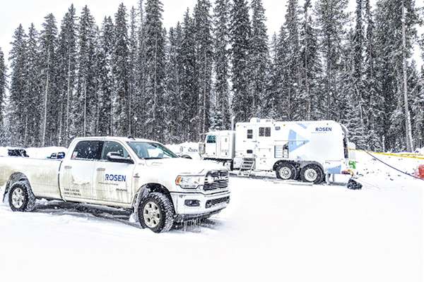 Pipeline and truck with ROSEN logo in snowy landscape in front of a forest.