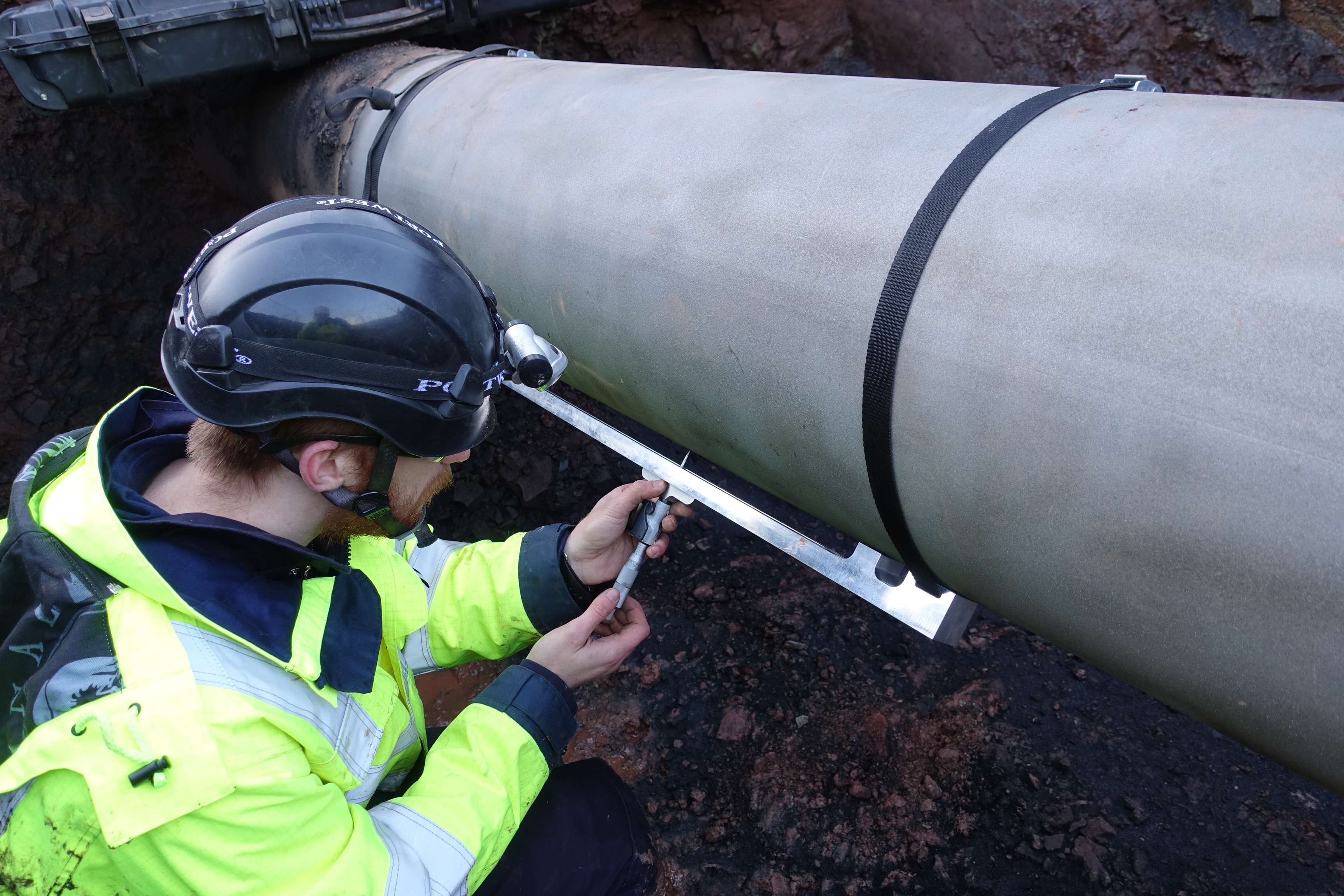 Man with safety hat inspects pipeline in field.
