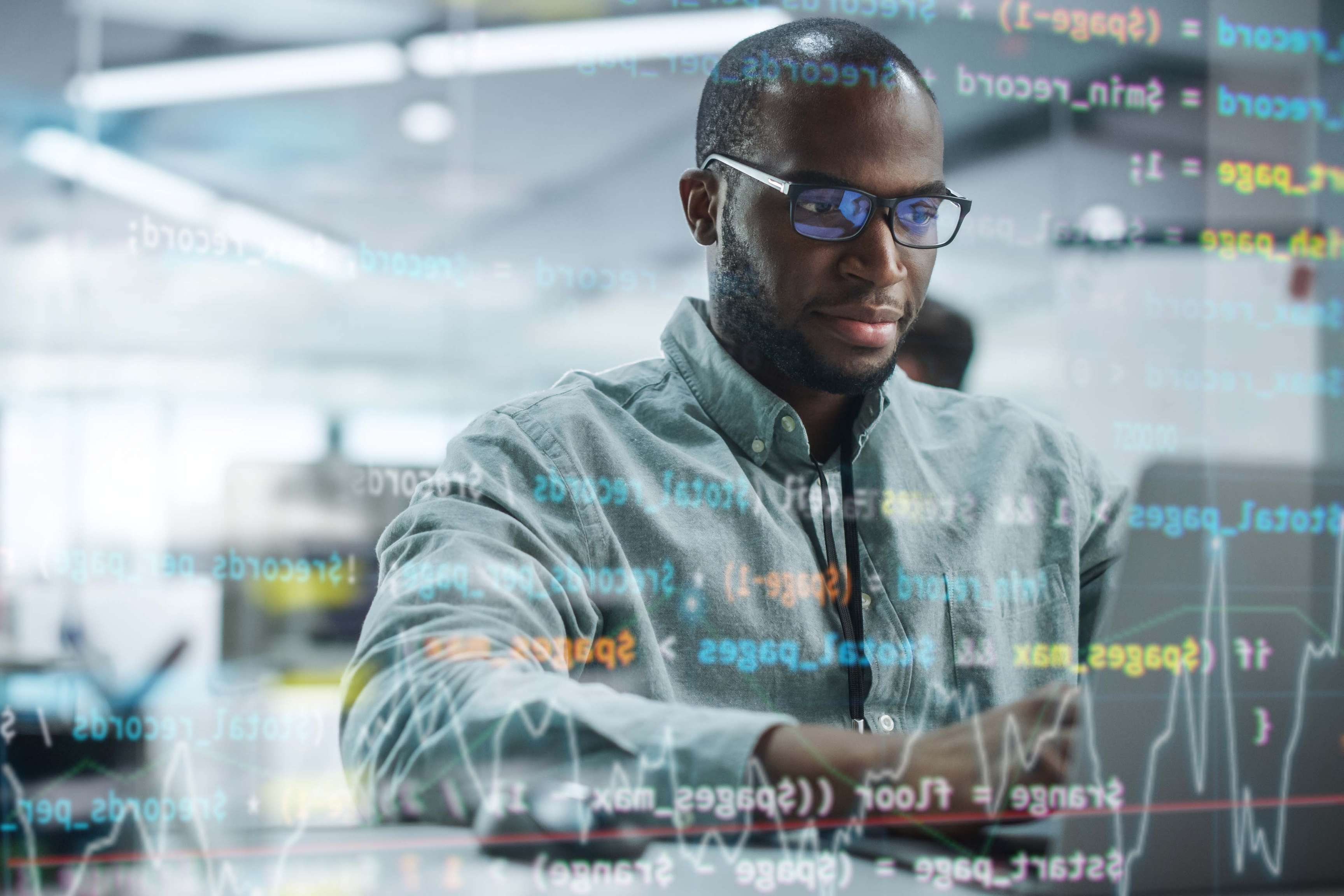 Portrait of man with glasses sitting in front of laptop and programming.