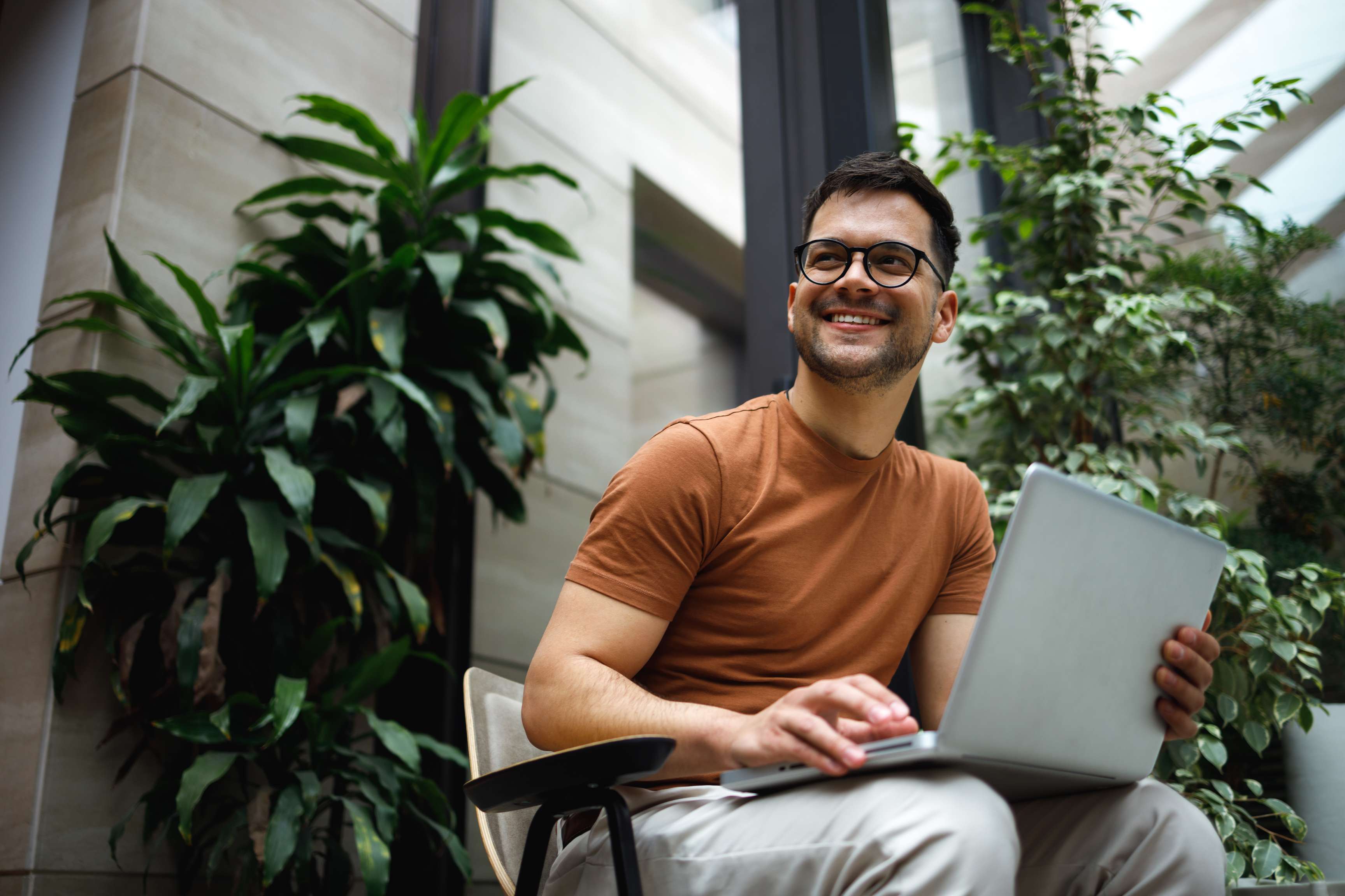 Man with glasses sits in front of a laptop and smiles while looking to the side.