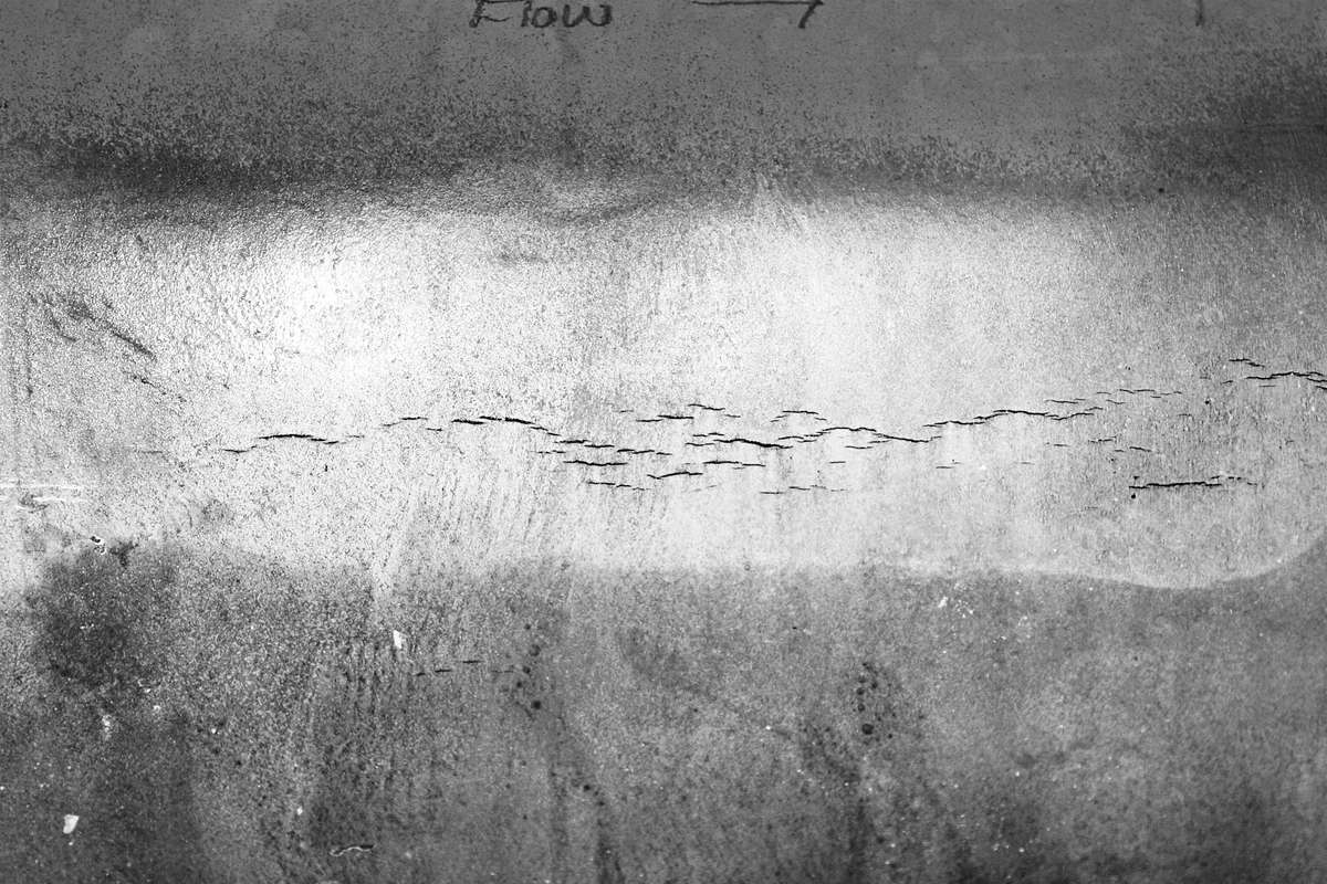 Close up of surface of a grey pipeline showing axial stress corrosion cracking.