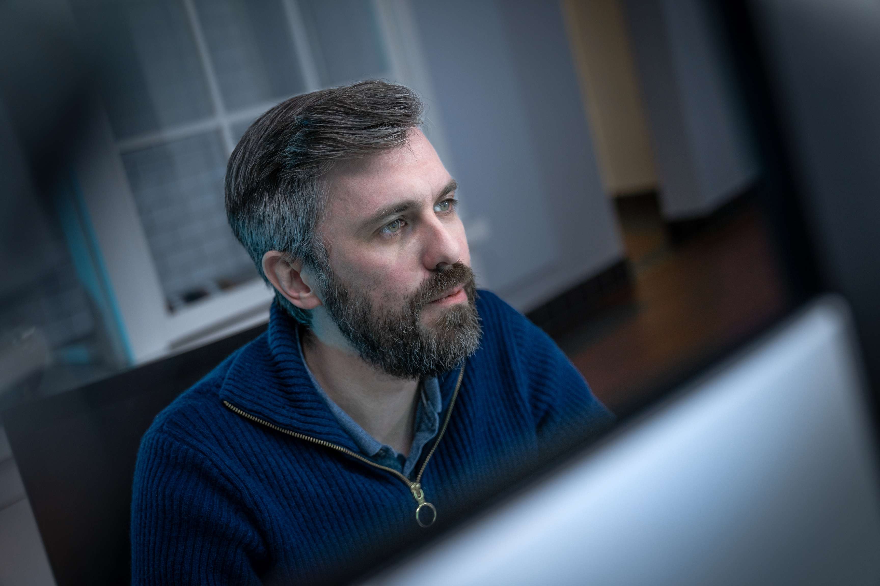 A man sits behind a computer screen and looks at the screen.