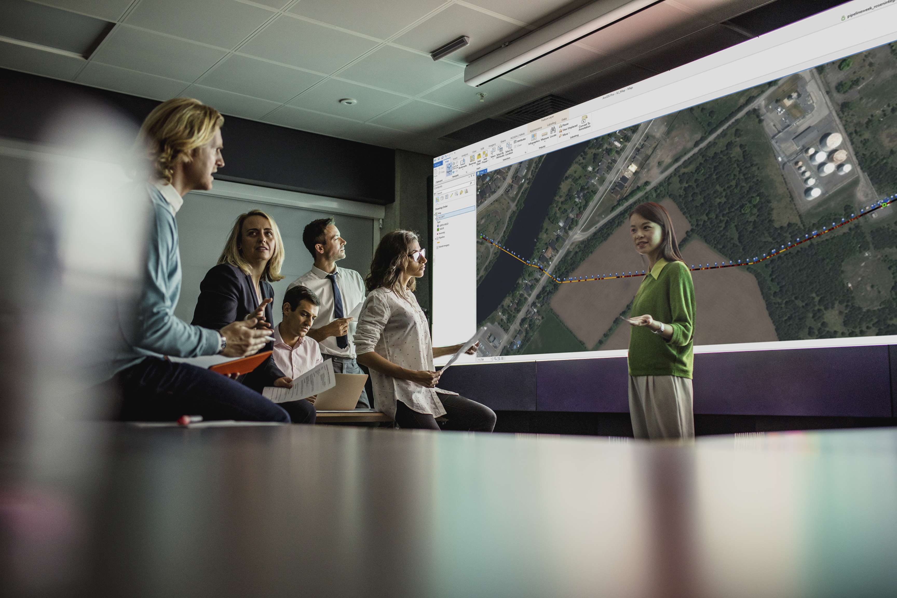 Several employees have gathered around a screen on which a pipeline is drawn on a map.