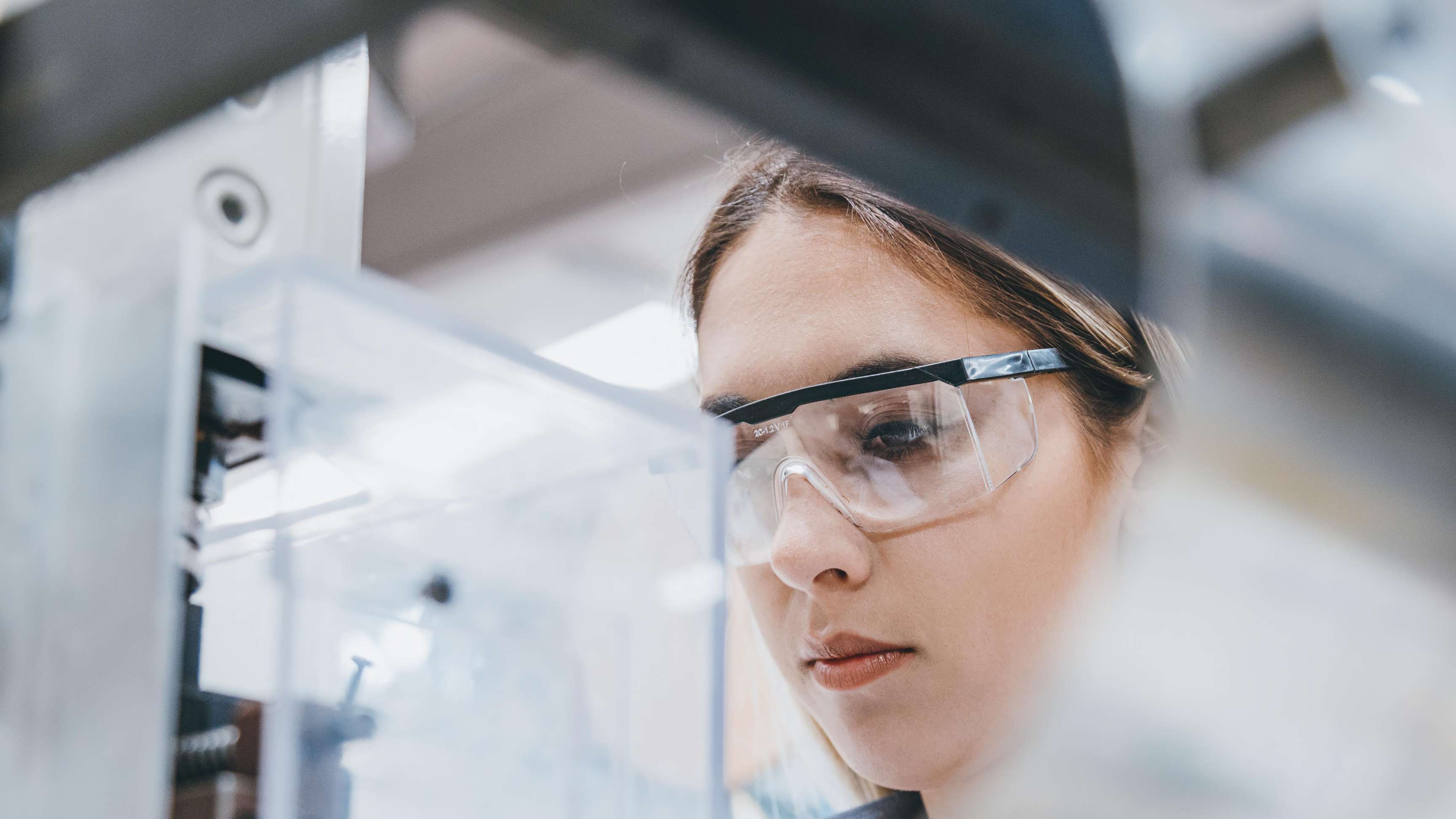 Woman with goggles in front of a device in the laboratory.