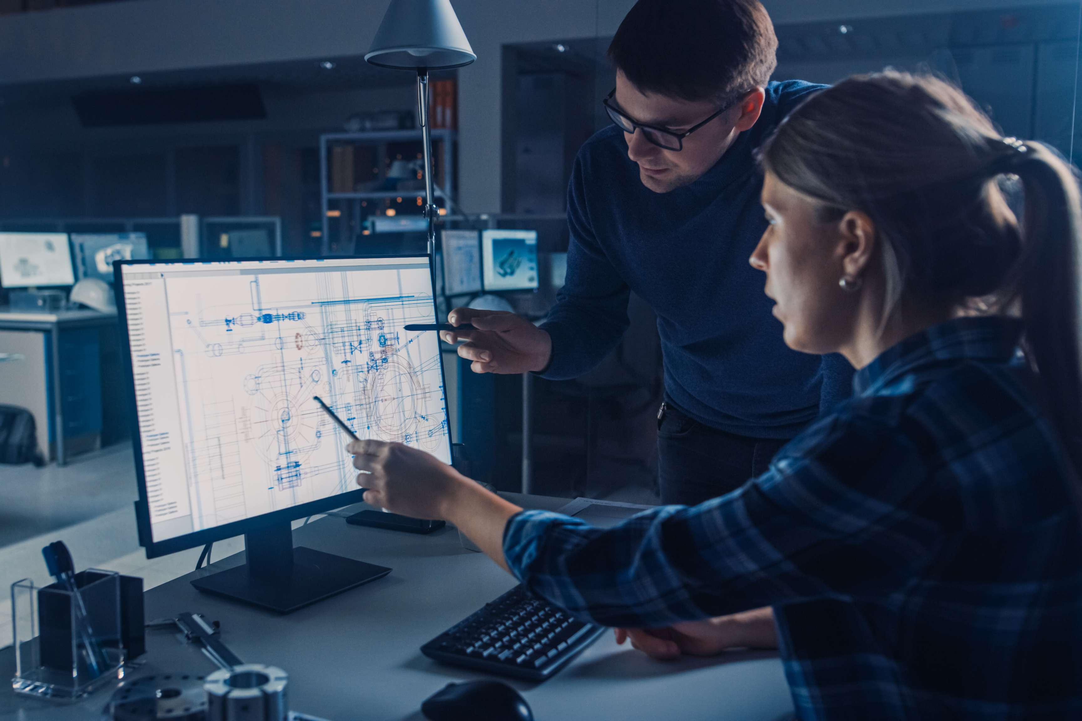 Two employees looking and pointing at spreadsheet on computer screen.