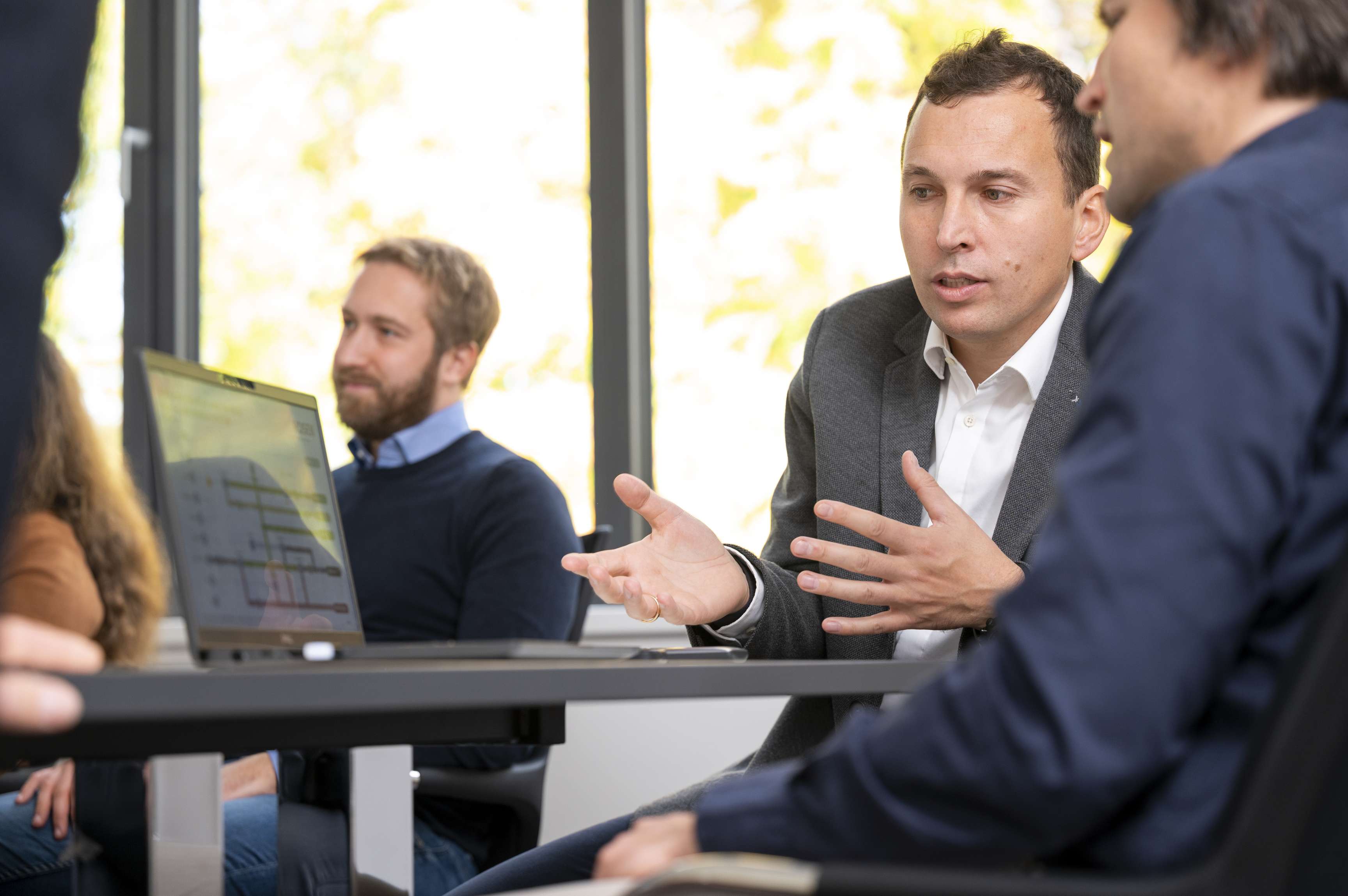 Two men are sitting at a table in front of a computer, looking at the screen and discussing.