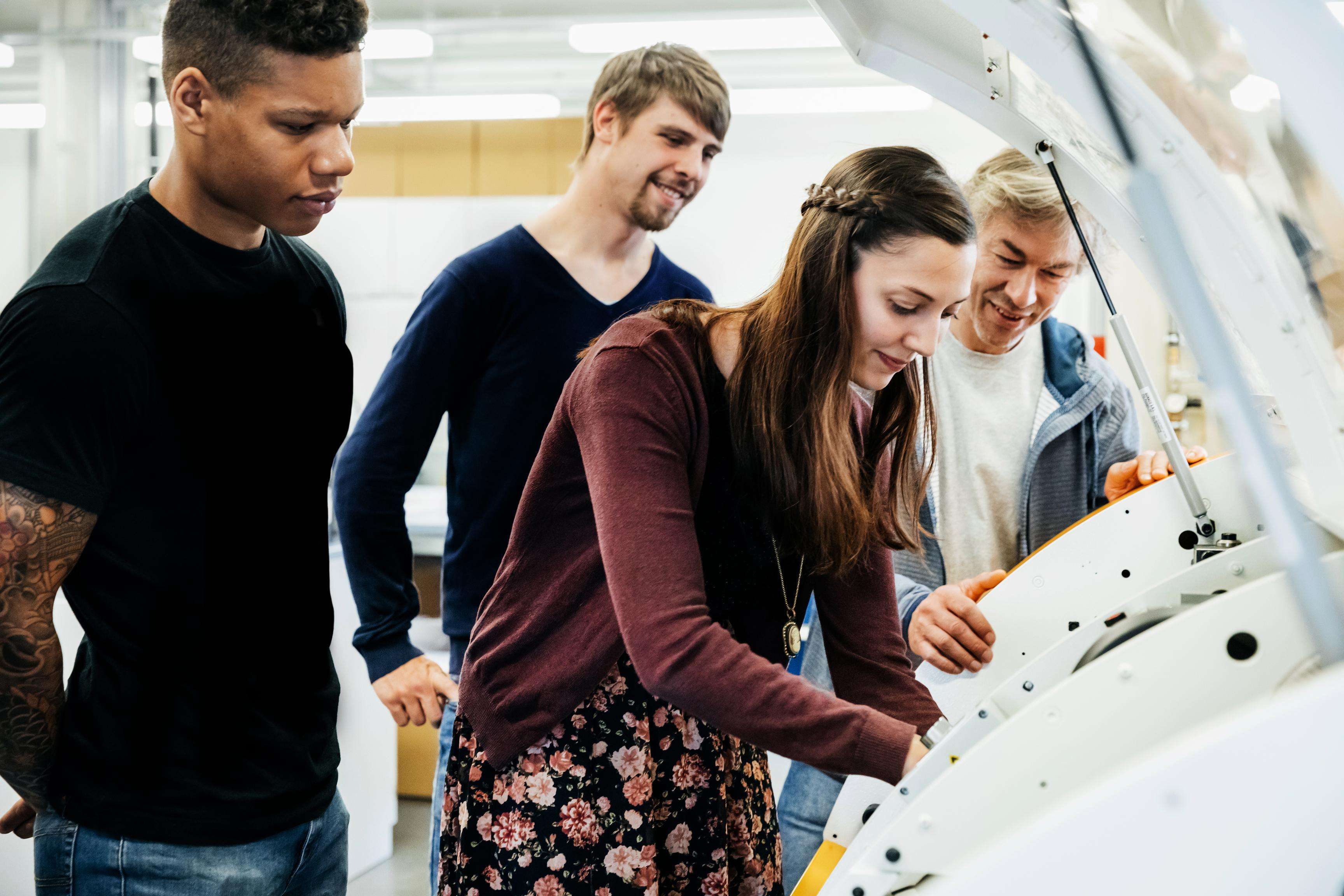 A group of students operating a complex machine, guided by their instructor.