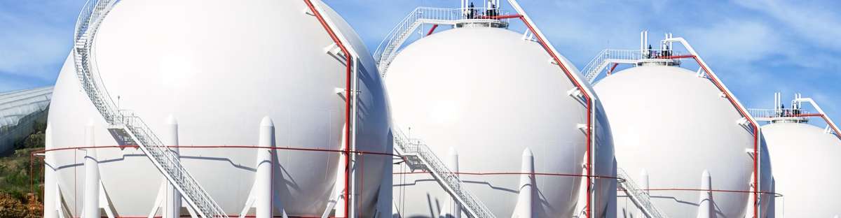 Seven round pressure vessels in a row with blue sky in the background.