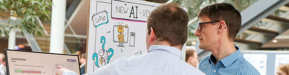 Two men standing in front of a screen and one is showing a graph to his colleague during the Creation Day 2024.