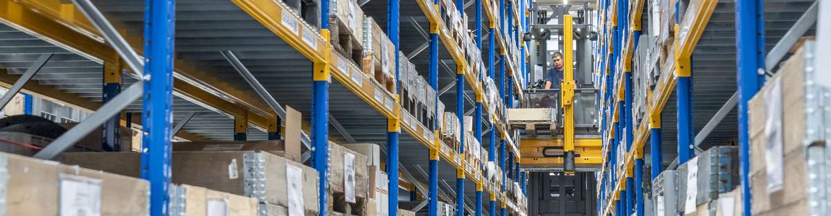 Ein Gabelstapler fährt zwischen Hochregalen hindurch.