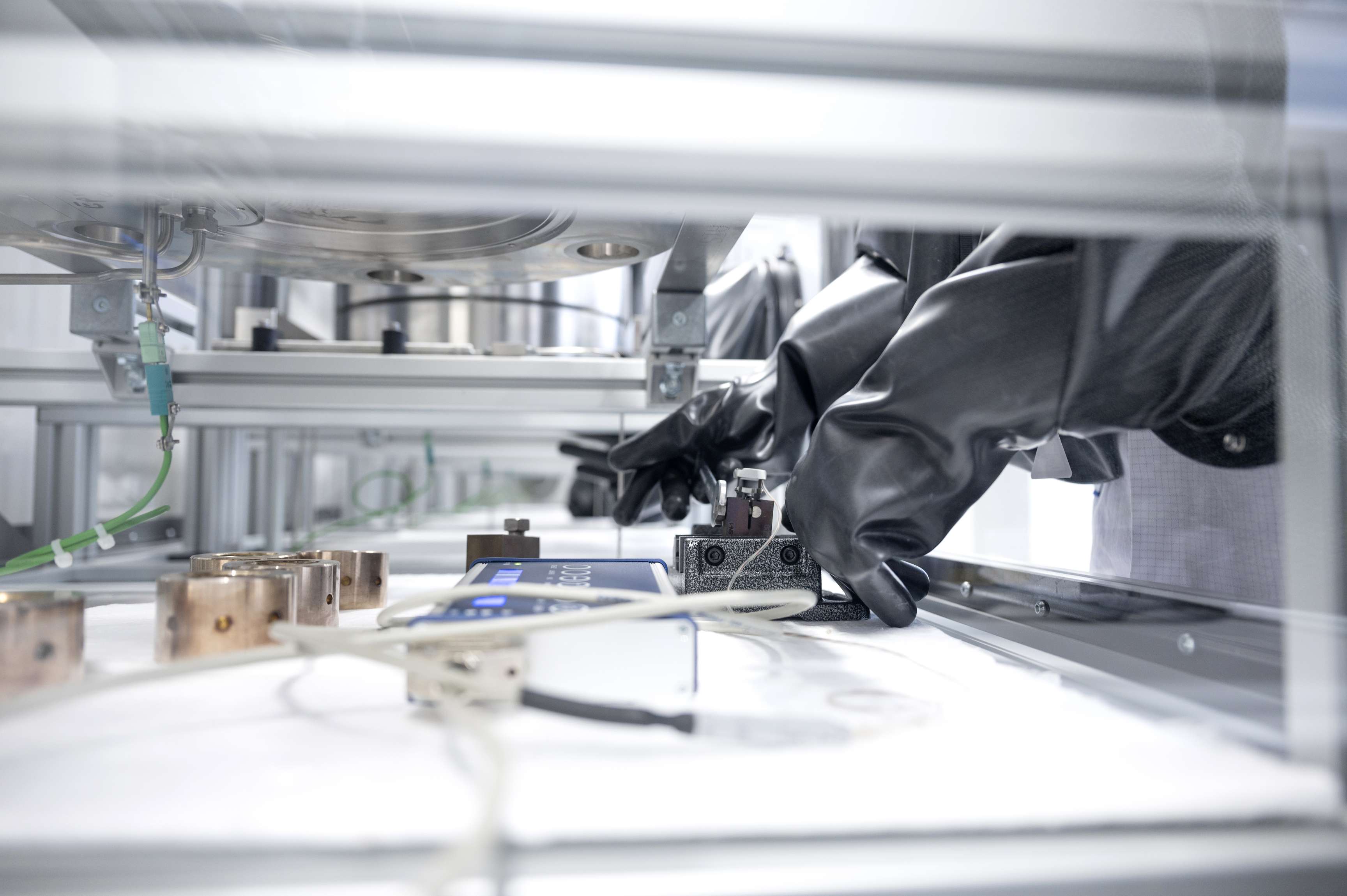 Black work gloves in front of a display connected to a device in a laboratory.