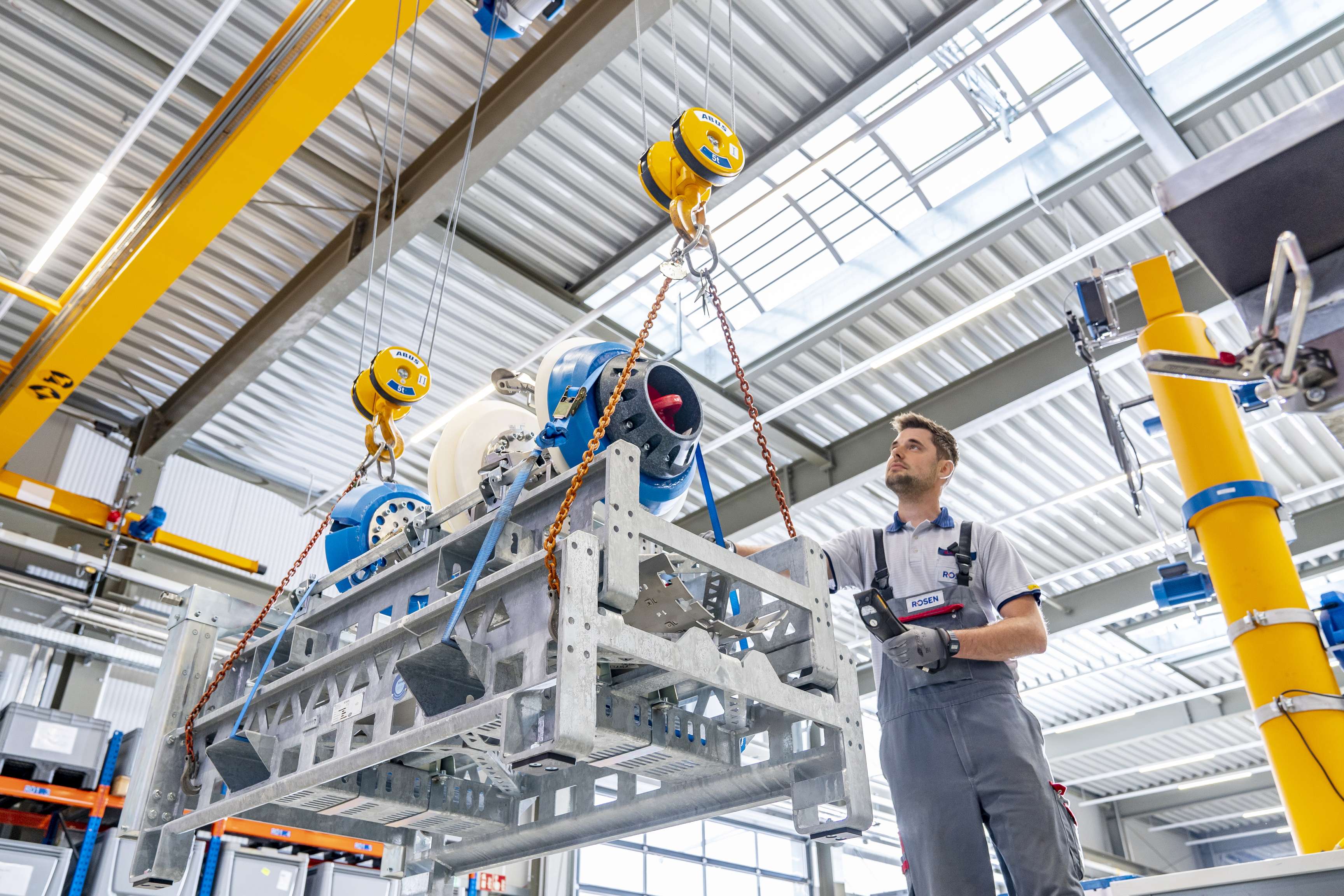 Montagearbeiter mit einem Tool vor sich auf einem Werkzeugträger, der von einem Kran angehoben wird