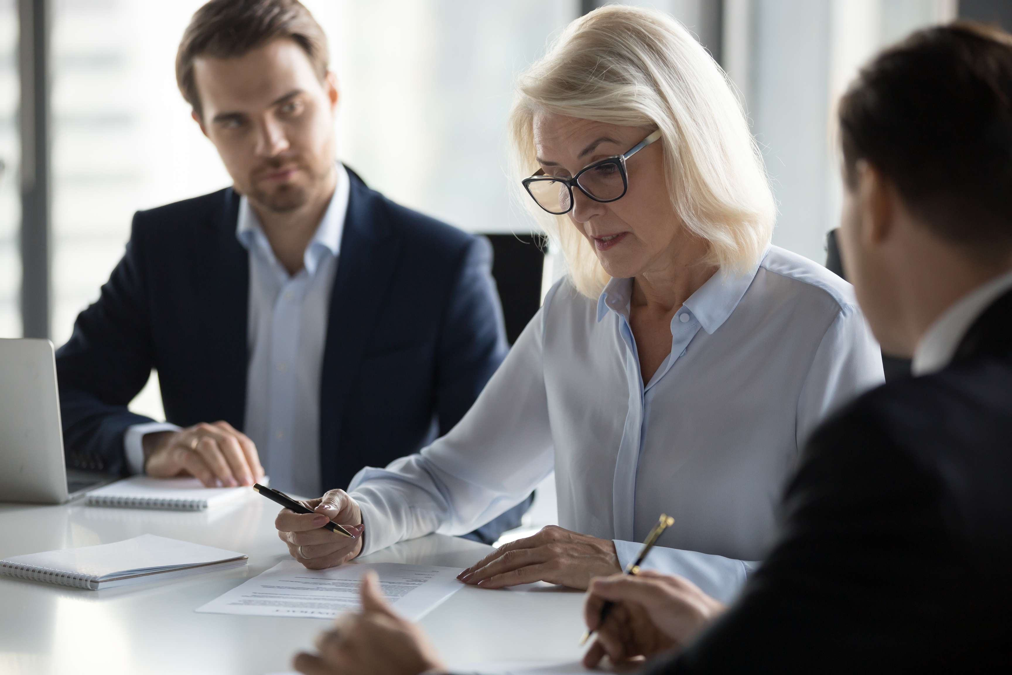 Three professionals sitting at a board room table reviewing a document.