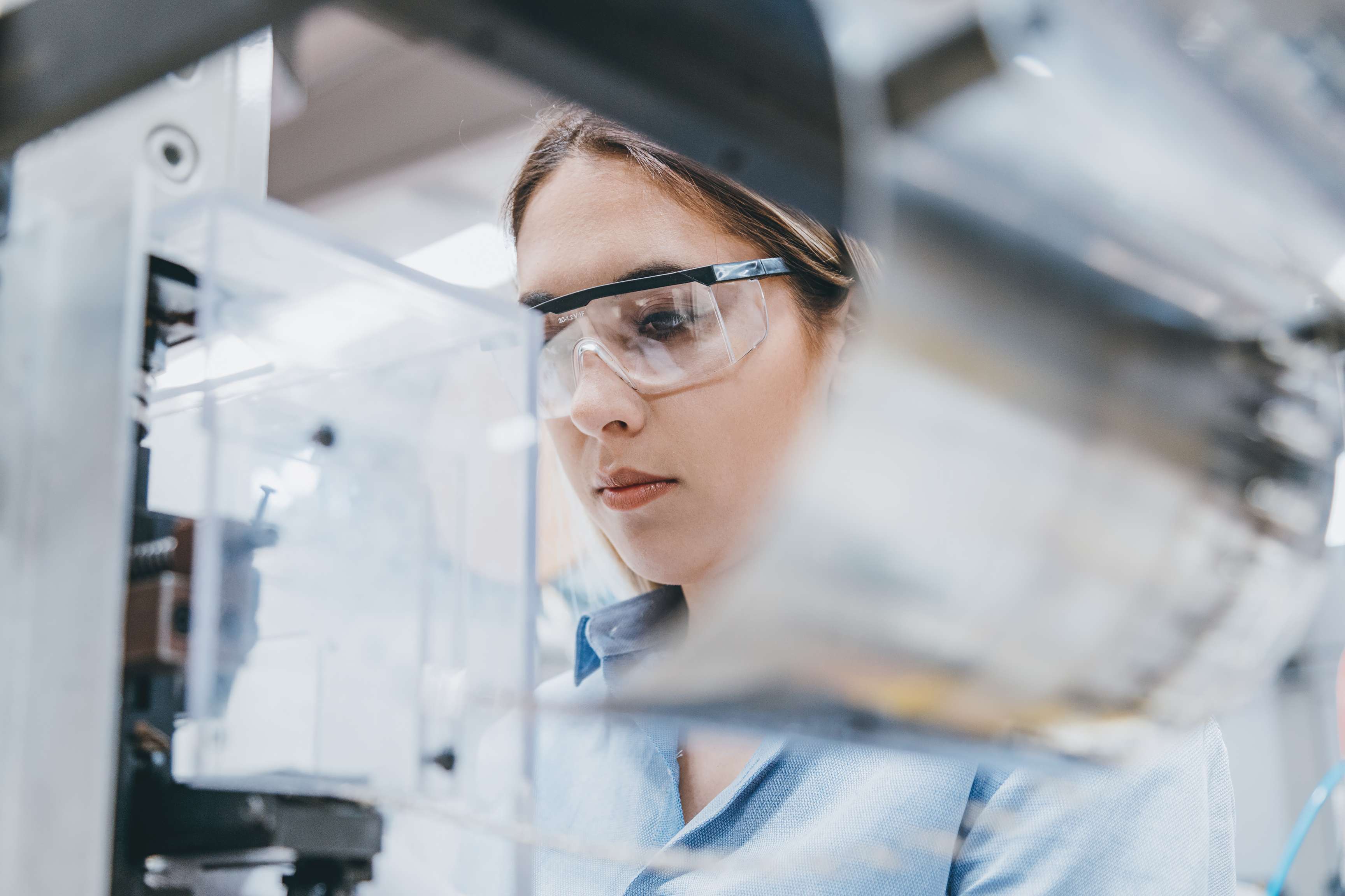 Woman with goggles in front of a device in the laboratory.