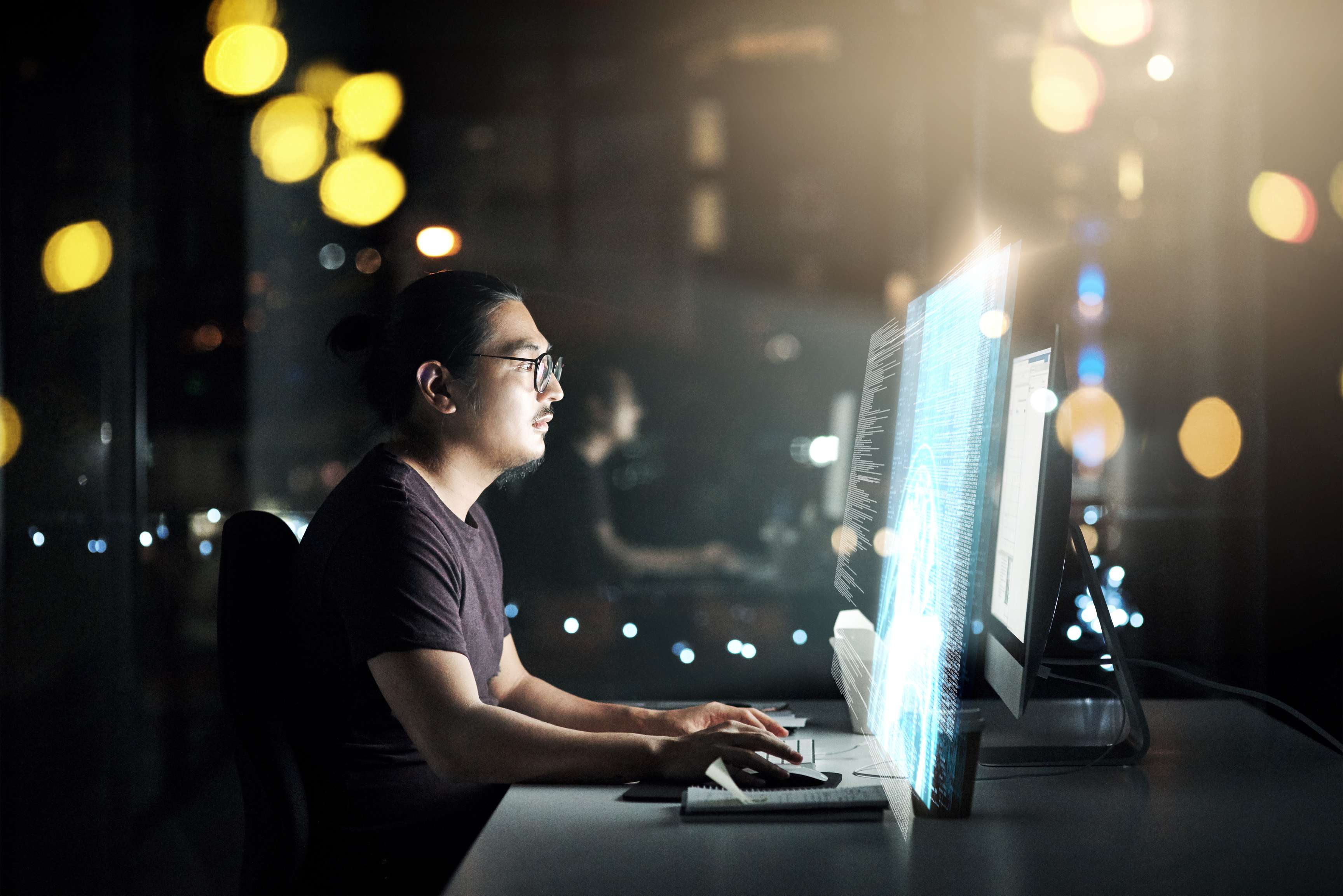 Side portrait of a man wearing glasses and sitting in front of several monitors.