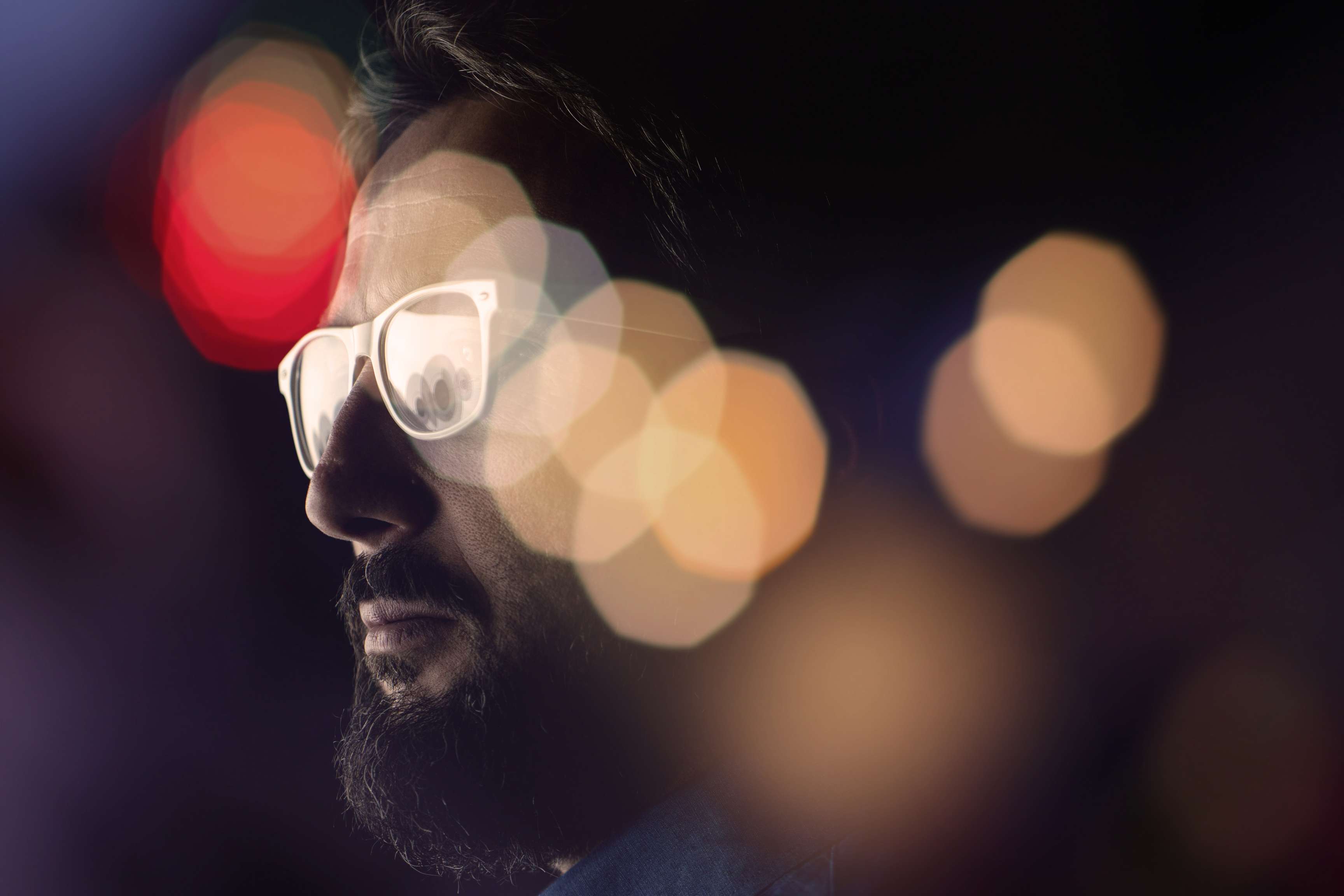 Portrait of man looking through window with light reflections through rain.