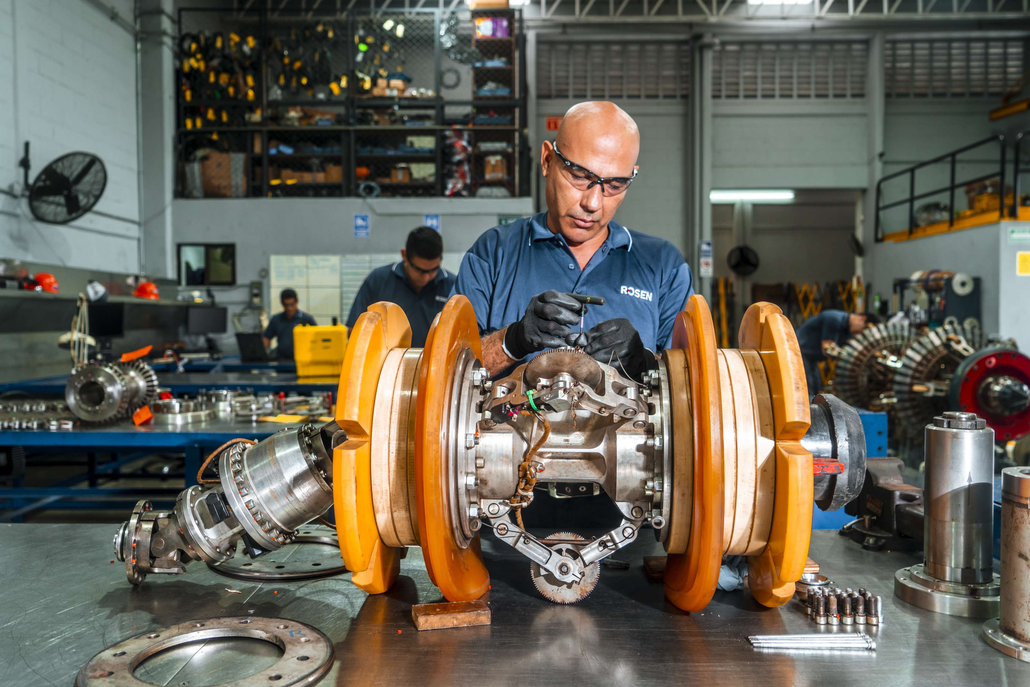 Man in a workshop setting wearing safety glasses servicing and assembling a ROSEN tool.