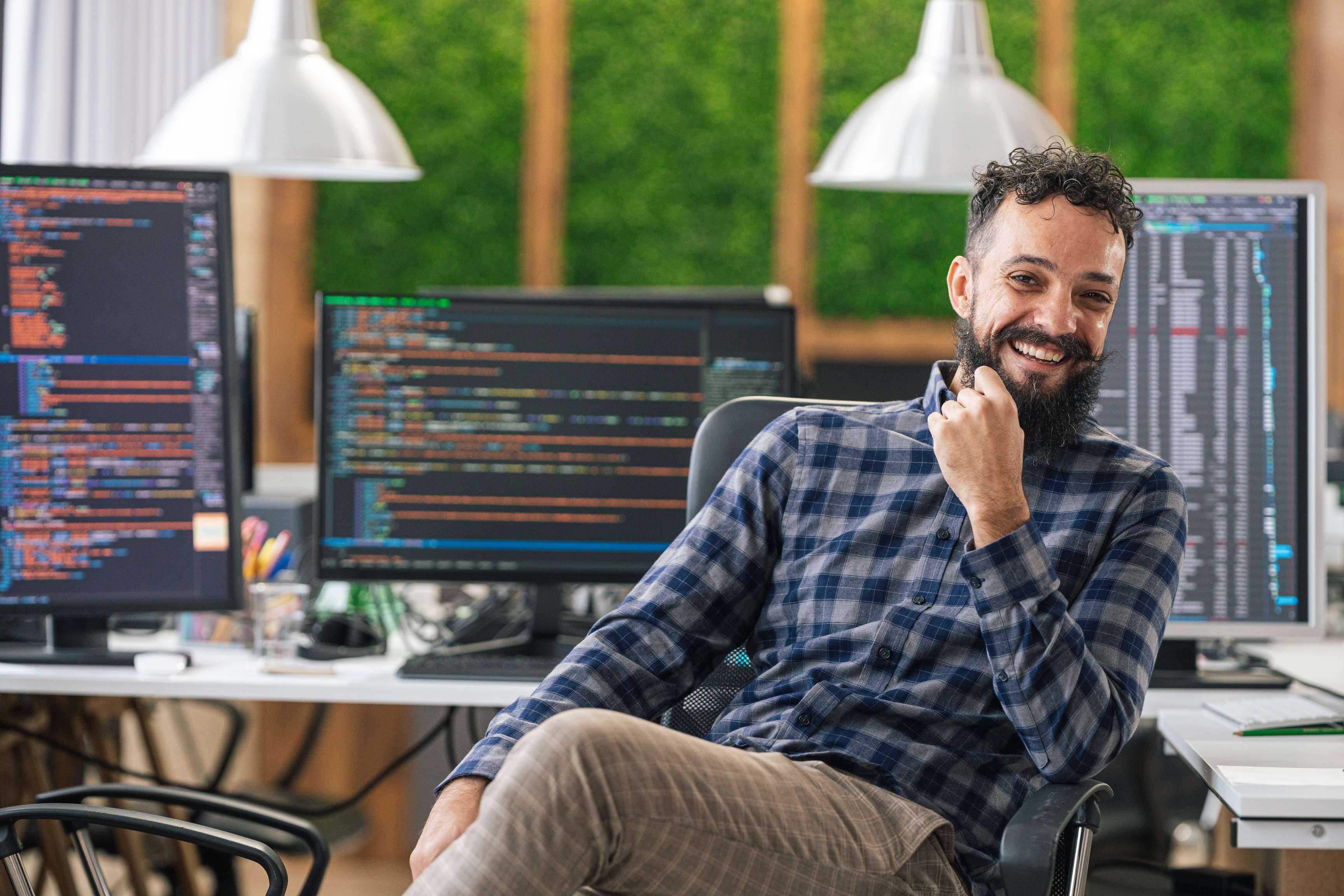 Portrait of smiling man sitting next to desktop computers displaying data and codes.